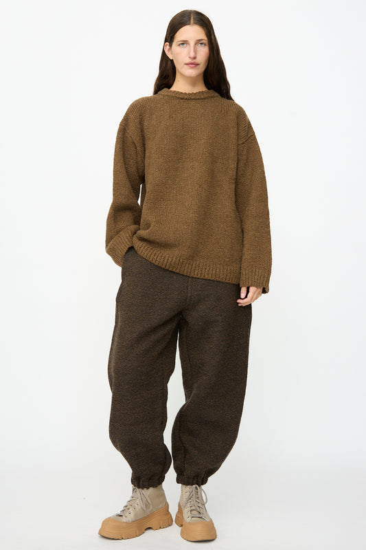 Person standing against a white background wearing a brown knit sweater, the Jamie Joggers in Blackmud from SONO with elastic cuffs, and beige lace-up boots.