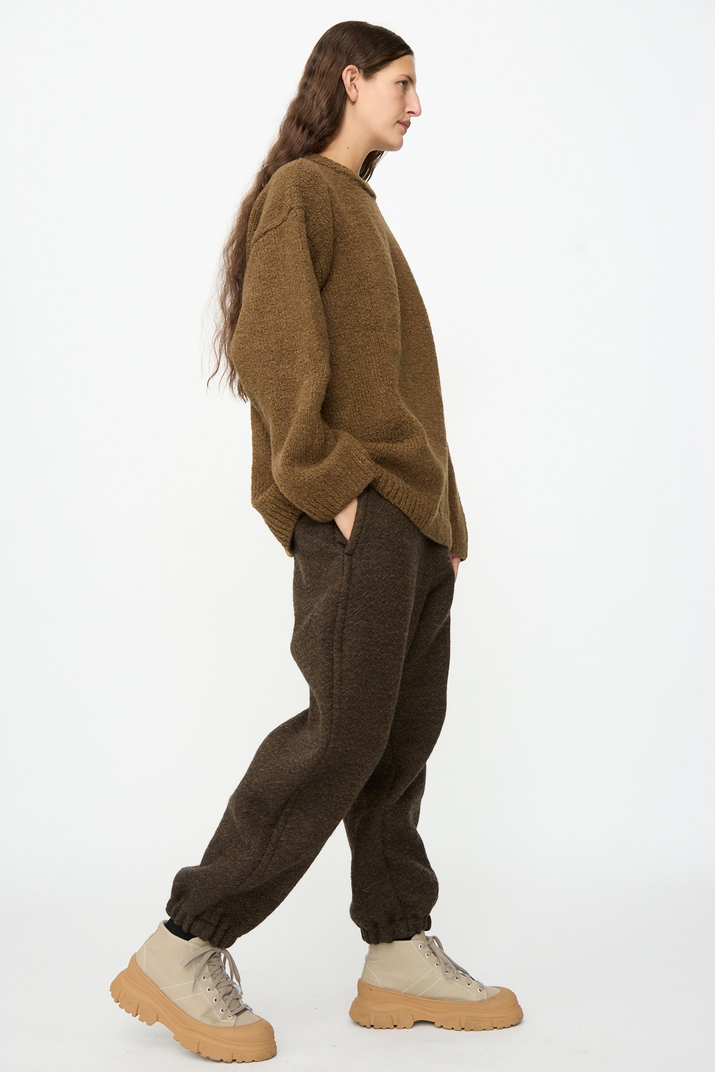 Person in a brown oversized sweater, SONO Jamie Joggers in Blackmud, and beige chunky boots stands in profile against a plain white background.