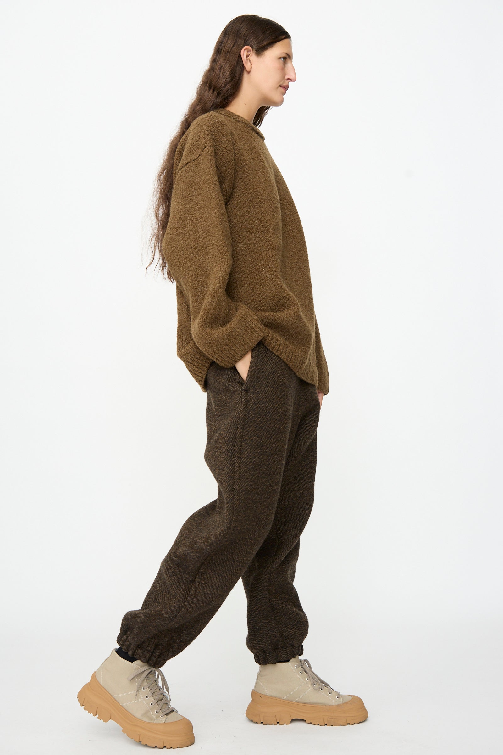 Person in a brown oversized sweater, SONO Jamie Joggers in Blackmud, and beige chunky boots stands in profile against a plain white background.