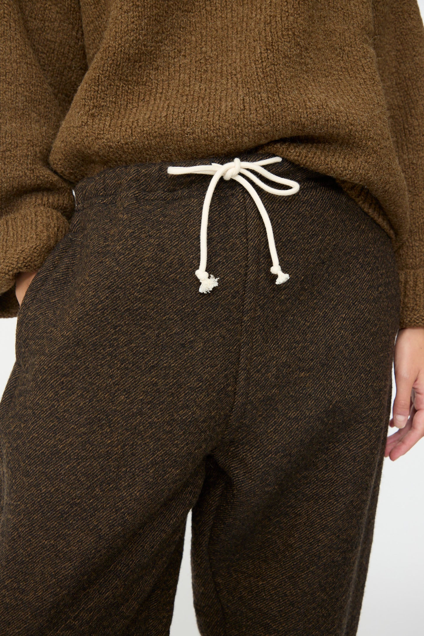 A person wearing the SONO Jamie Joggers in Blackmud, paired with a brown textured sweater, shown from the midsection to upper thighs.