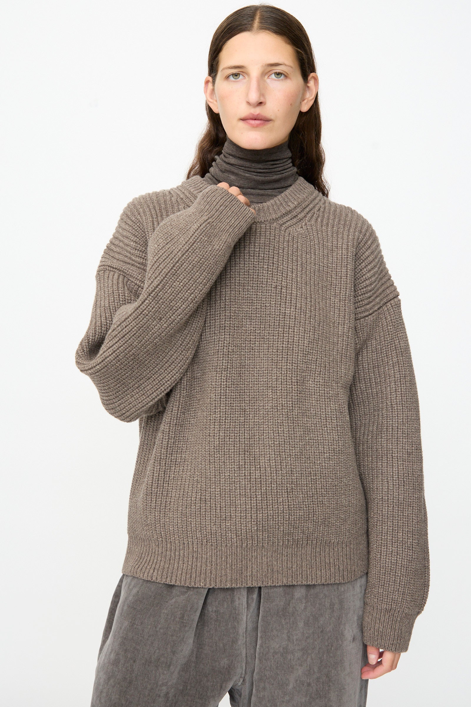 Person wearing the SONO Joel Jumper in Smoke—an oversized, ribbed knit wool pullover—layered over a gray turtleneck and gray pants, standing against a plain white background.