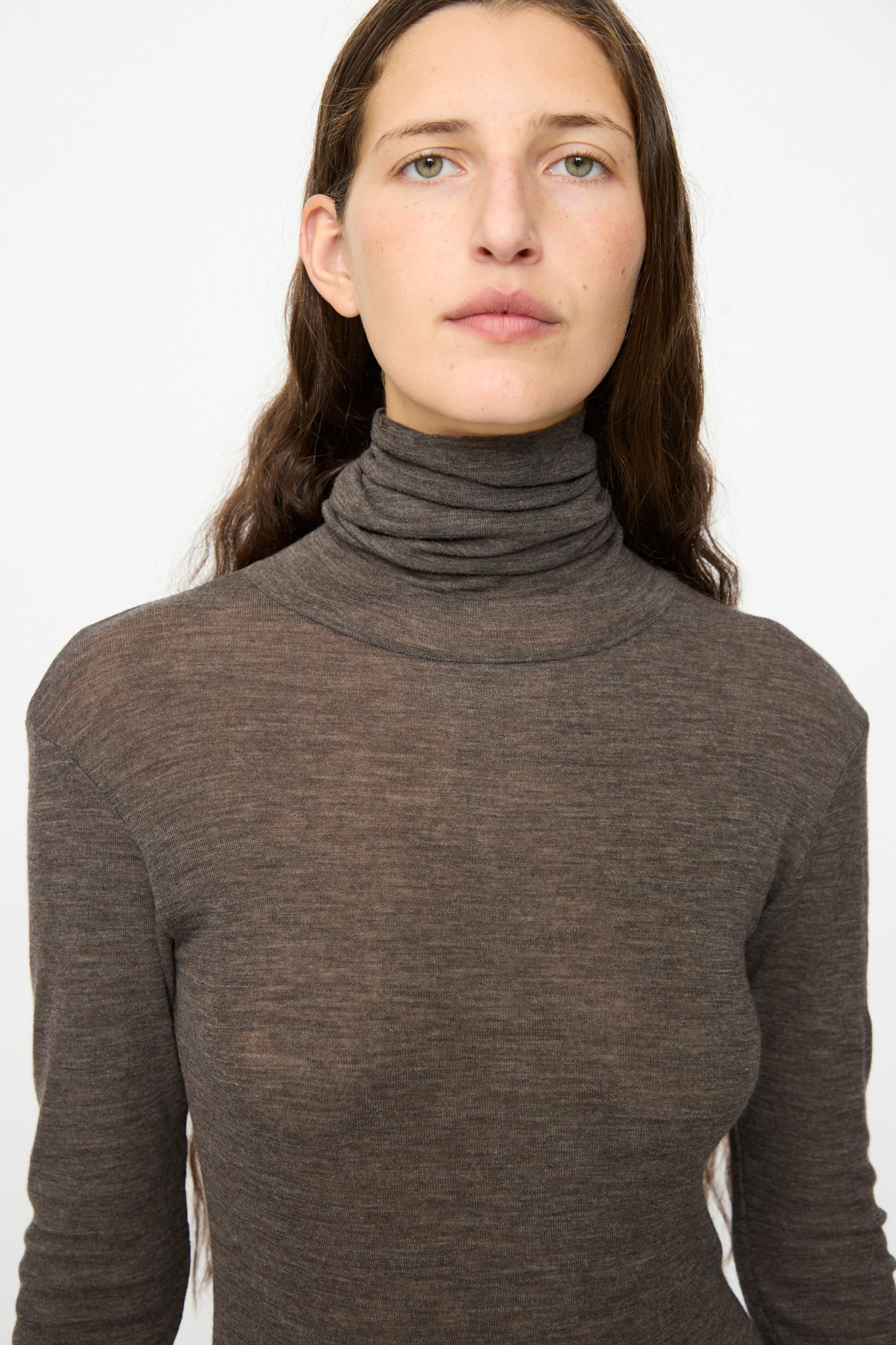 A person with long brown hair wears the SONO Roberta Rollneck in Charcoal, a slim fit sheer turtleneck, and looks directly at the camera against a plain white background.