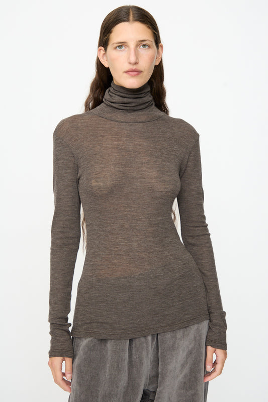 A person with long brown hair wears the SONO Roberta Rollneck in Charcoal, styled with loose gray pants, standing against a plain white background.