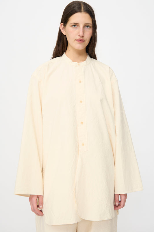 A person with long brown hair wears the SONO Shaman Shirt in Ecru, an oversized long sleeve button-up with a stand collar, standing against a plain white background.