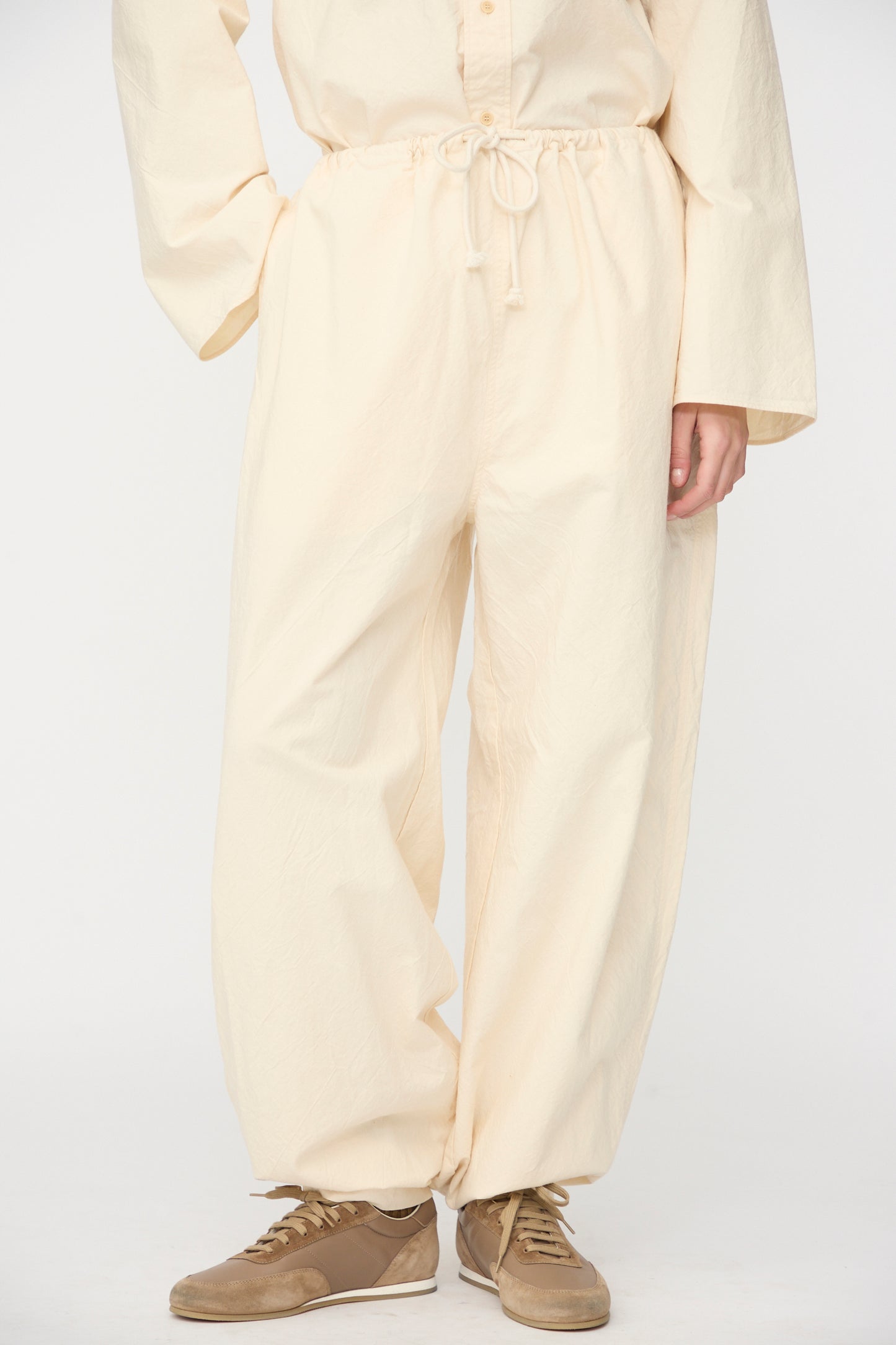 Model wears the SONO Sol Snowpant in Ecru—oversized, organic cotton pants with a drawstring waist—paired with brown sneakers against a plain white background.