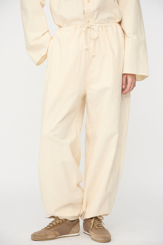 Model wears the SONO Sol Snowpant in Ecru—oversized, organic cotton pants with a drawstring waist—paired with brown sneakers against a plain white background.