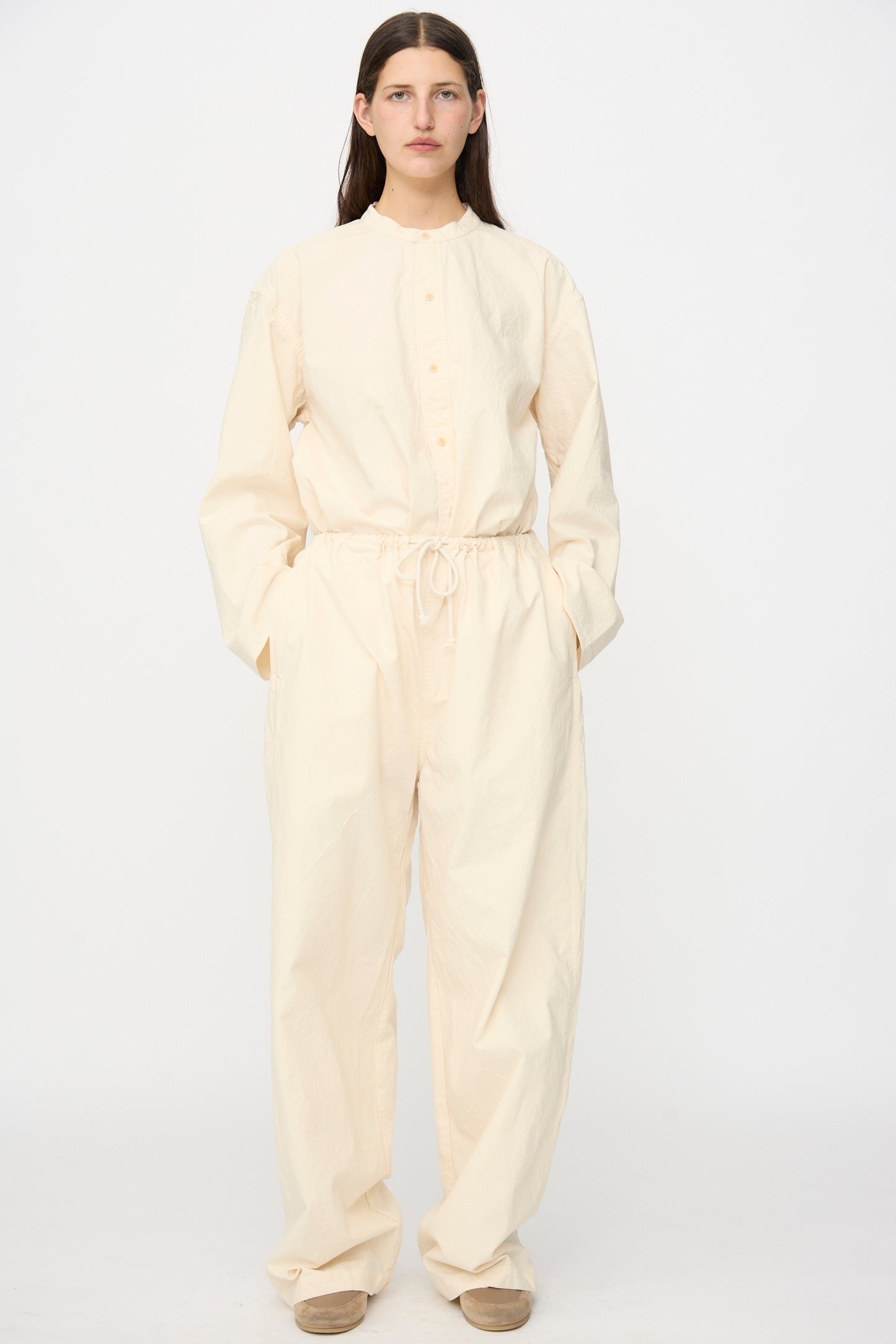 A person stands facing forward, hands in pockets, wearing the SONO Sol Snowpant in Ecru against a plain white background. The organic cotton pants feature a loose fit with wide, oversized legs and long sleeves for a relaxed look.