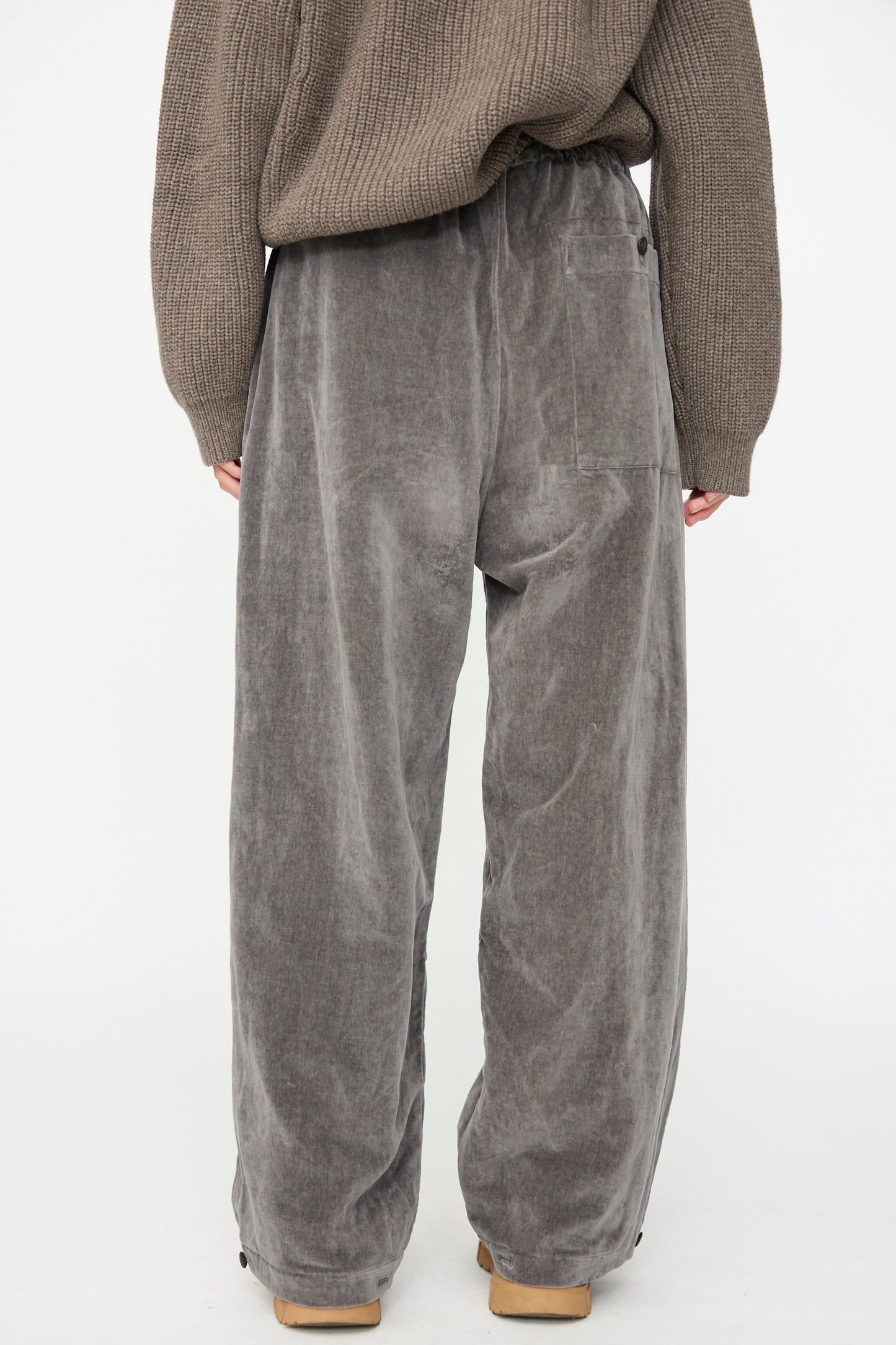 A person wearing the SONO Sol Snowpant in Elephant—an oversized velvet pant with a drawstring waist—stands with their back to the camera against a plain white background.