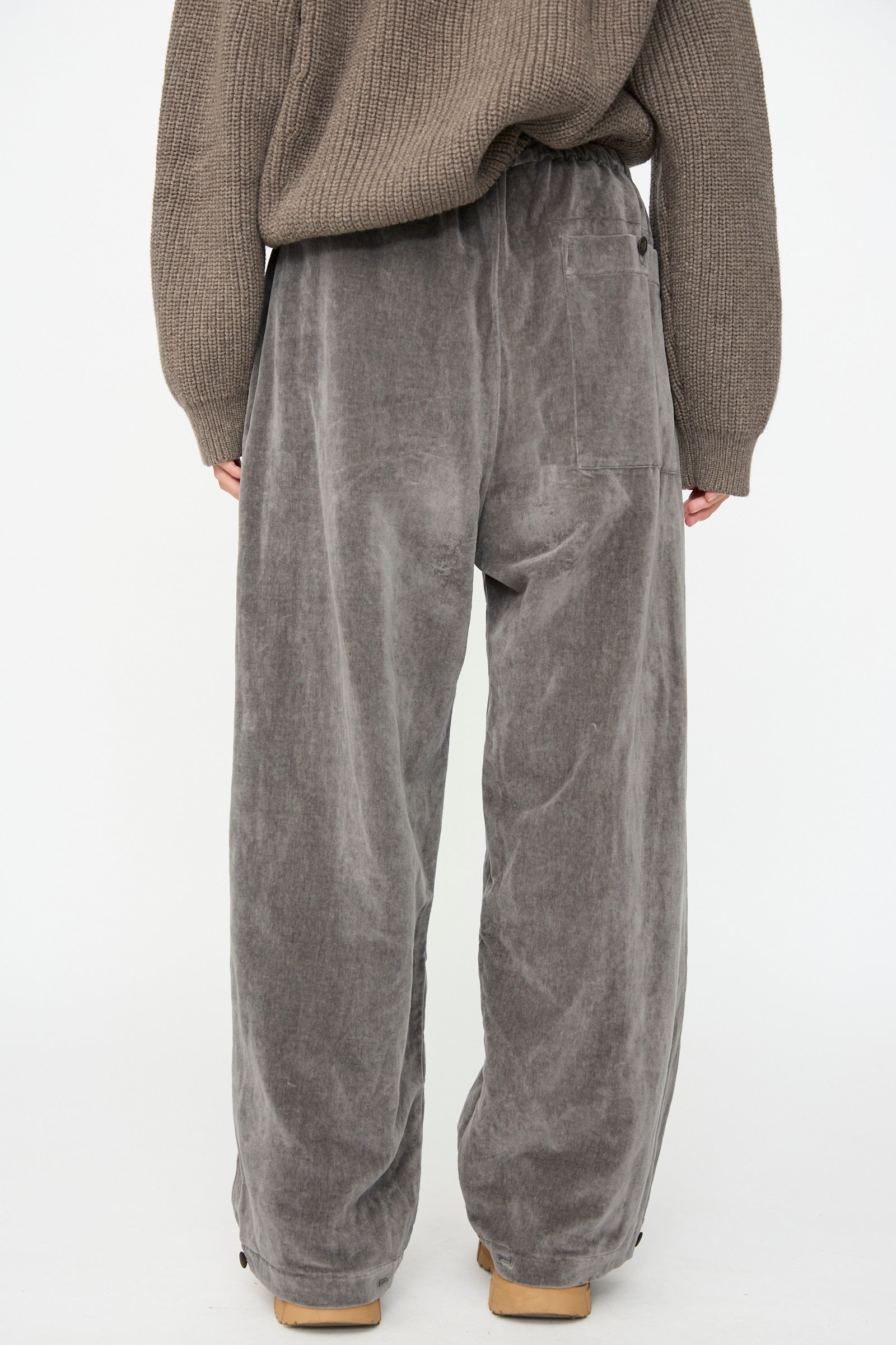 A person wearing the SONO Sol Snowpant in Elephant—an oversized velvet pant with a drawstring waist—stands with their back to the camera against a plain white background.
