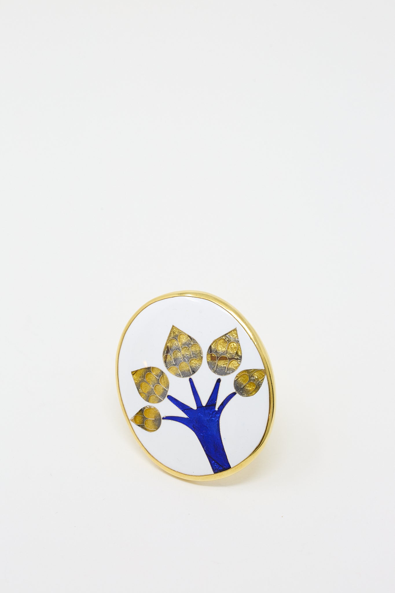 A circular brooch with a gold-colored rim featuring a blue tree design and yellow accents against a white background, inspired by the Byzantine cloisonné technique, from Sofio Gongli's Ring in Tree collection.