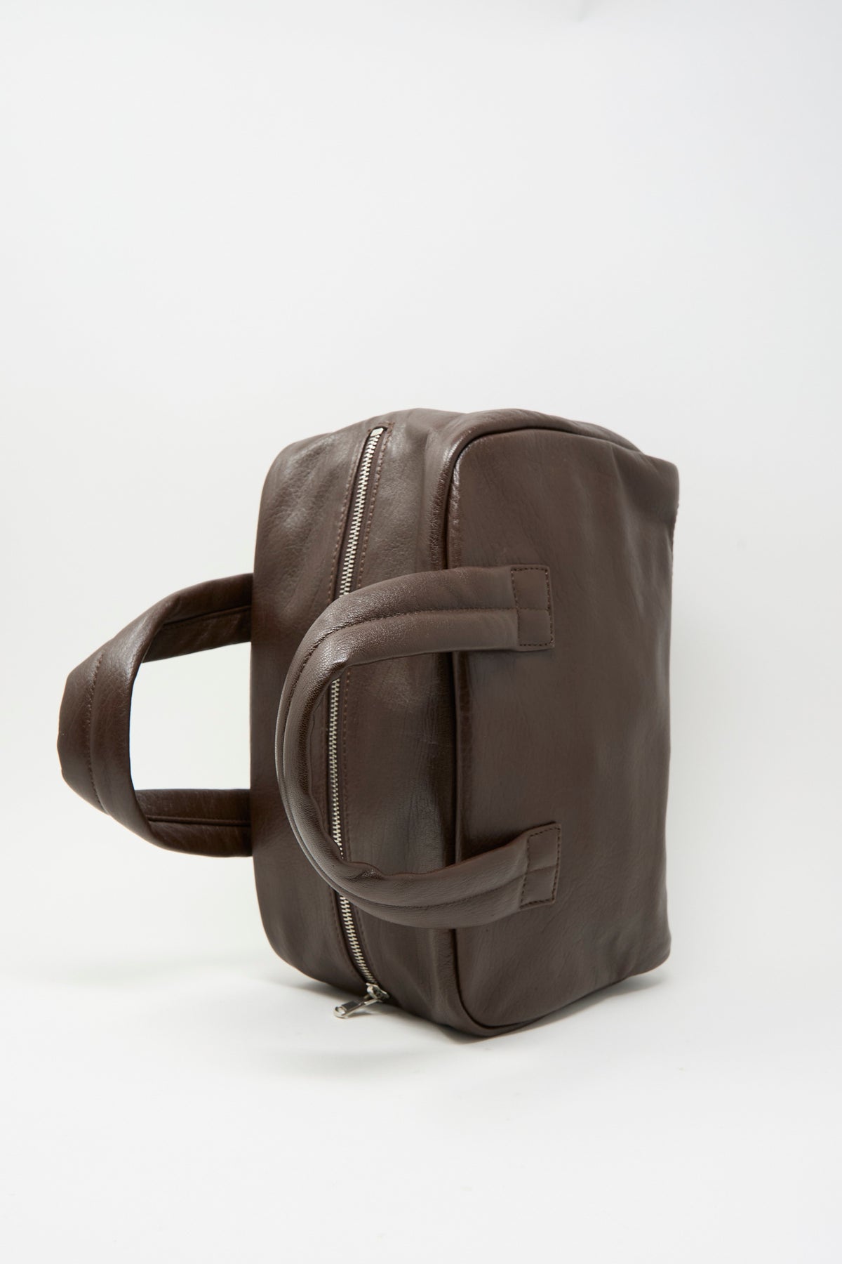 Side view of a dark brown Sabina Leather The Bowling Bag featuring a top zipper and two sturdy handles.