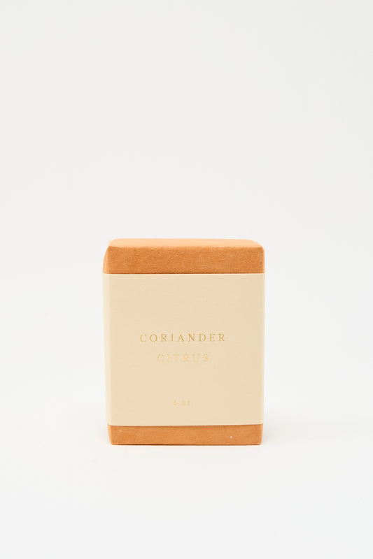 A handcrafted SAIPUA Olive Oil Bar Soap in Coriander Citrus, with a tan label reading "Coriander Citrus 6 oz.," stands upright against a white background. Made in New York, it features a refreshing blend of essential oils.