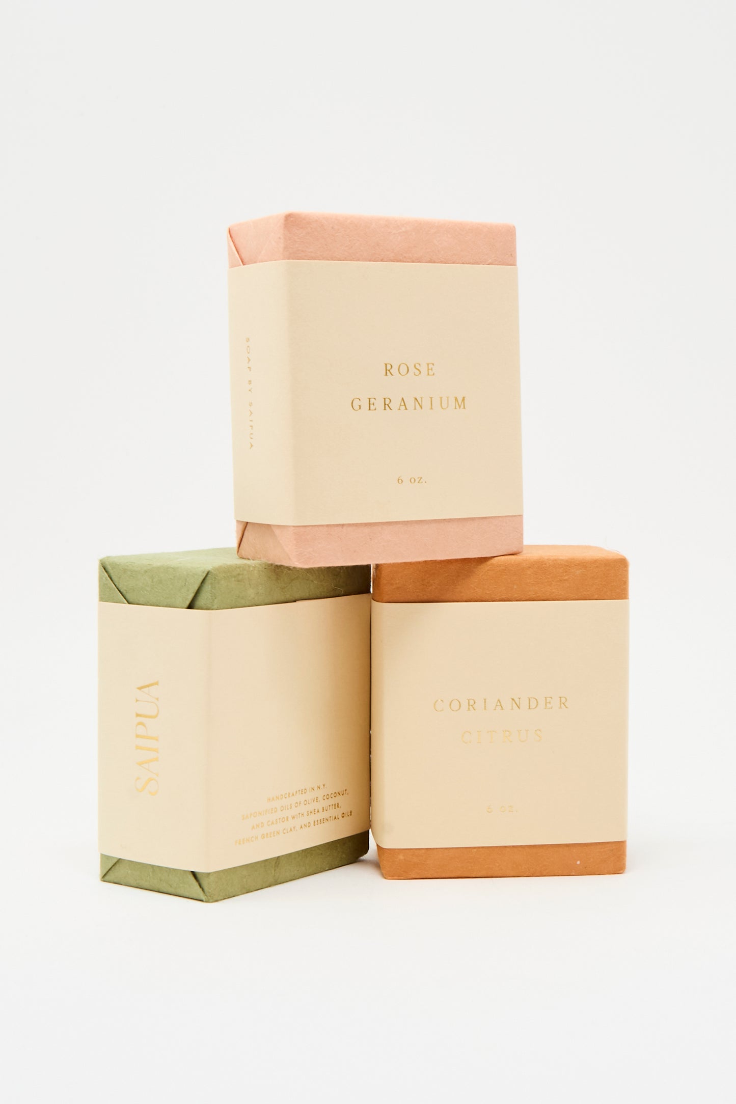 Three rectangular SAIPUA Olive Oil Bar Soaps are stacked with "Rose Geranium," "SÁVILA," and "Coriander Citrus" on neutral packaging, featuring essential oils, all set against a white background.