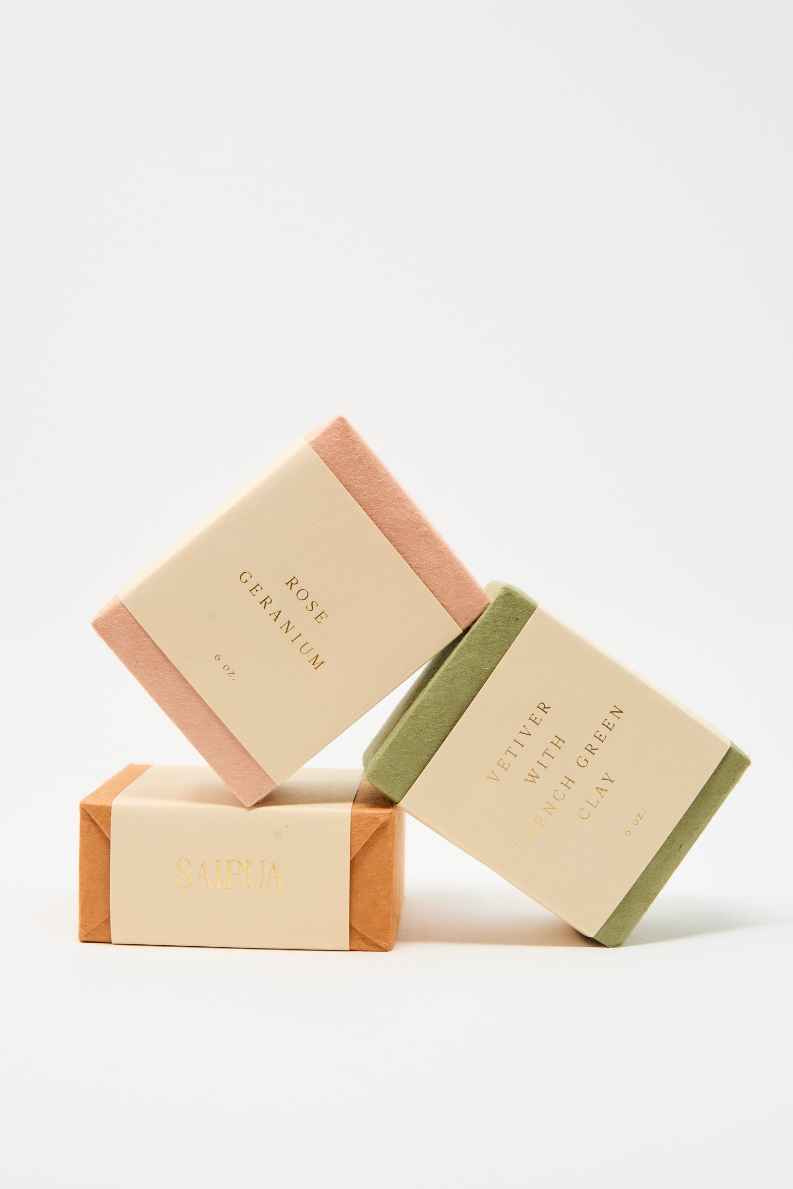 Three SAIPUA Olive Oil Bar Soaps, including the Rose Geranium scent, are stacked with minimalist labels against a white background; scents include rose geranium, vetiver with French green clay, and an unlabeled orange floral blend.