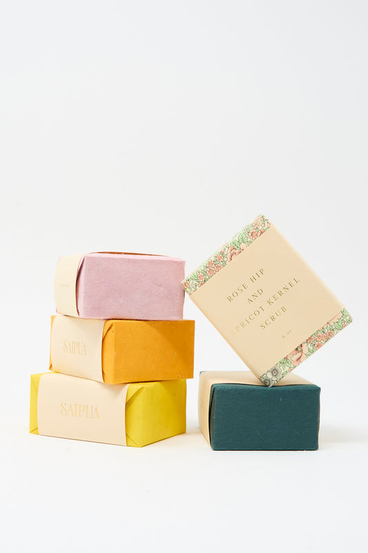 Five pastel-hued rectangular bars of SAIPUA soaps, including the "Rose Hip and Apricot Kernel Scrub Soap," are neatly stacked against a plain white background.