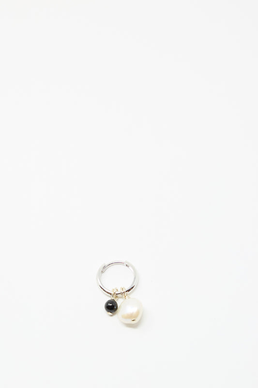 The Santangelo Baba Earring in Baby Black Agate features two dangling charms—a black agate bead and a white pearl— displayed on a plain white background.