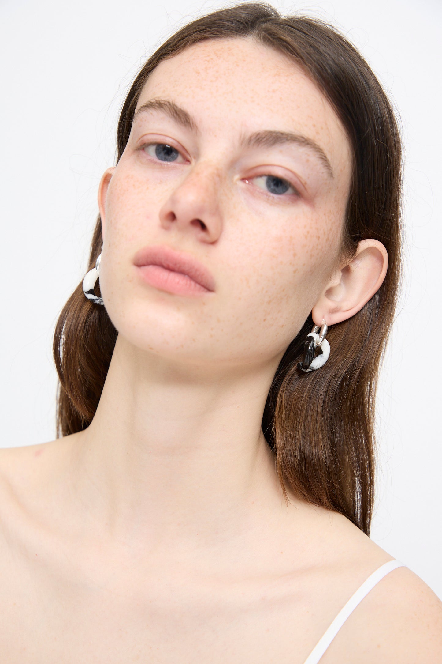 A woman with long brown hair wears Santangelo's Bad Orb Earrings in Zebra Jasper and a white top, gazing slightly upwards against a plain white background.