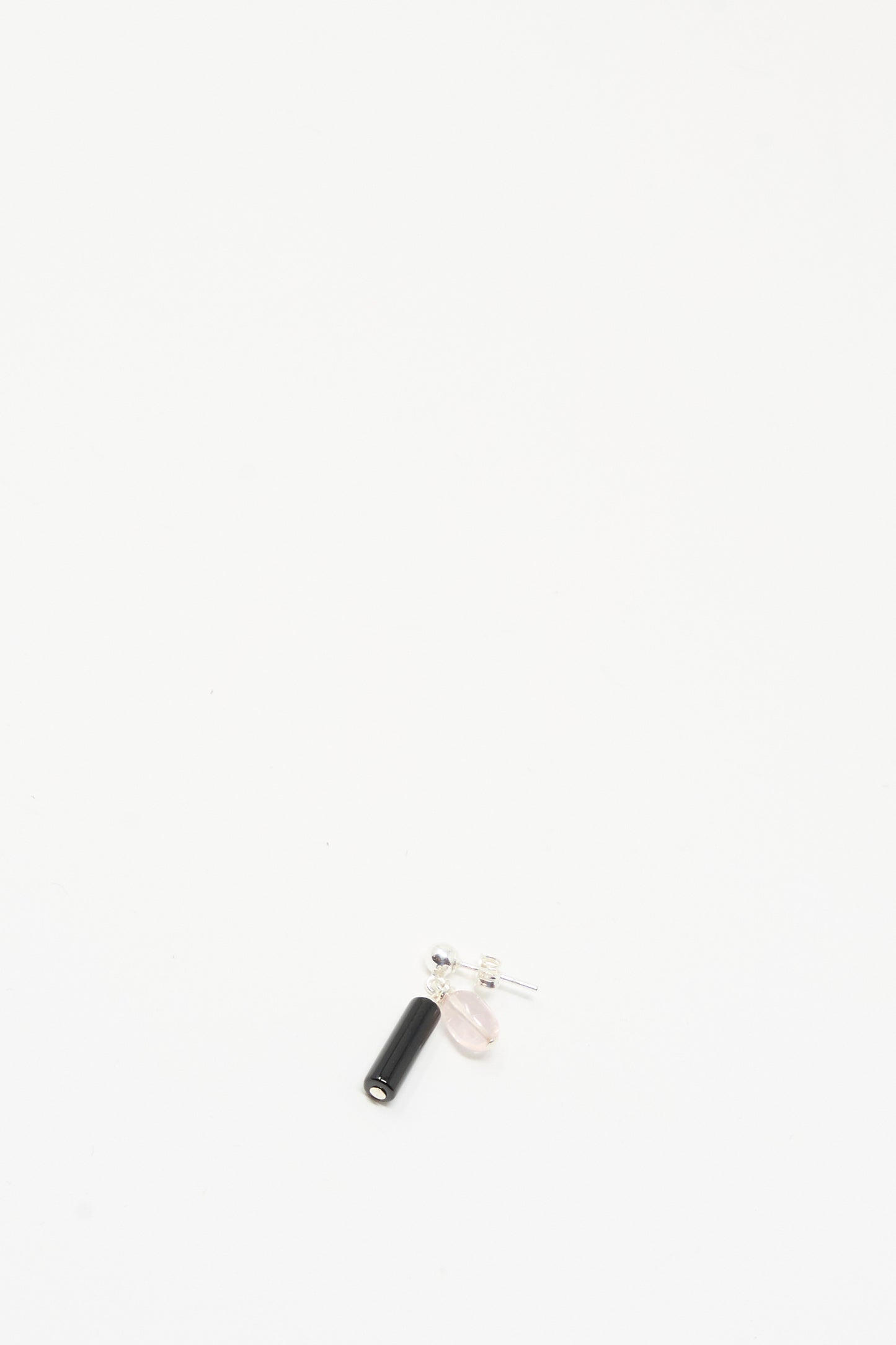 The Santangelo Bebecita Single Earring in Rose Quartz Onyx Drop is a small stud earring with a sterling silver post, featuring a black onyx cylinder and pale pink oval bead, shown on a plain white background.