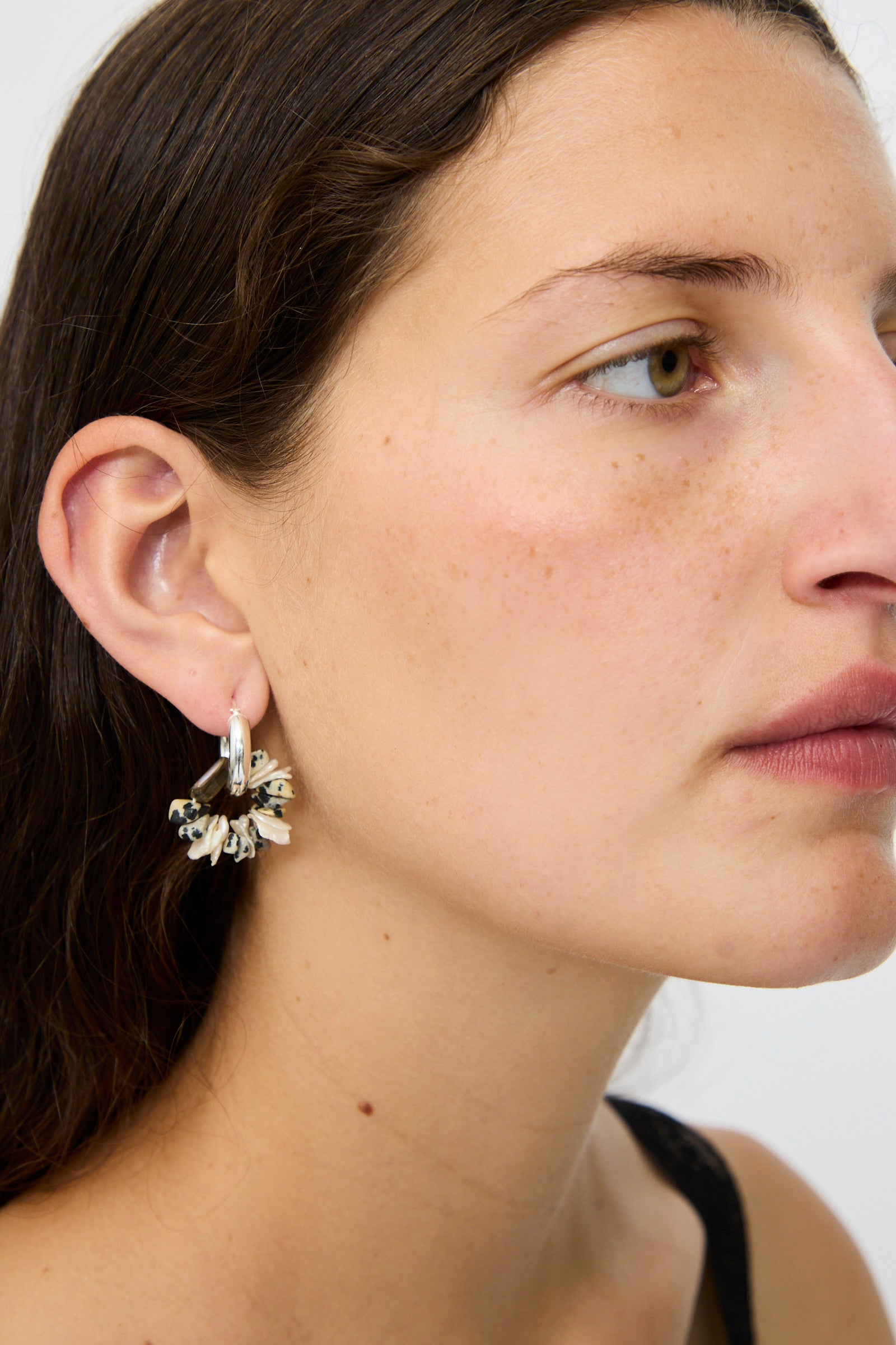 A woman with long brown hair wears Santangelo's Che Bomba Earrings in Abalone Hoop in her left ear, shown in close-up side profile against a plain background.