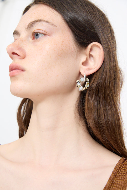A woman with long brown hair, wearing a brown top and Santangelo’s Che Bomba Earrings in Abalone Hoop, looks off to the side.