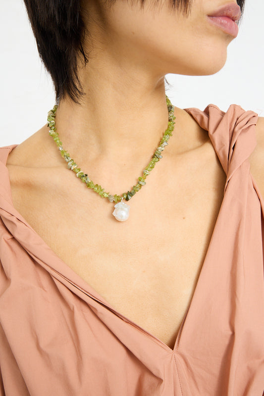 Woman wearing a Santangelo Kitano Necklace in Green with a large pearl pendant, dressed in a peach blouse.