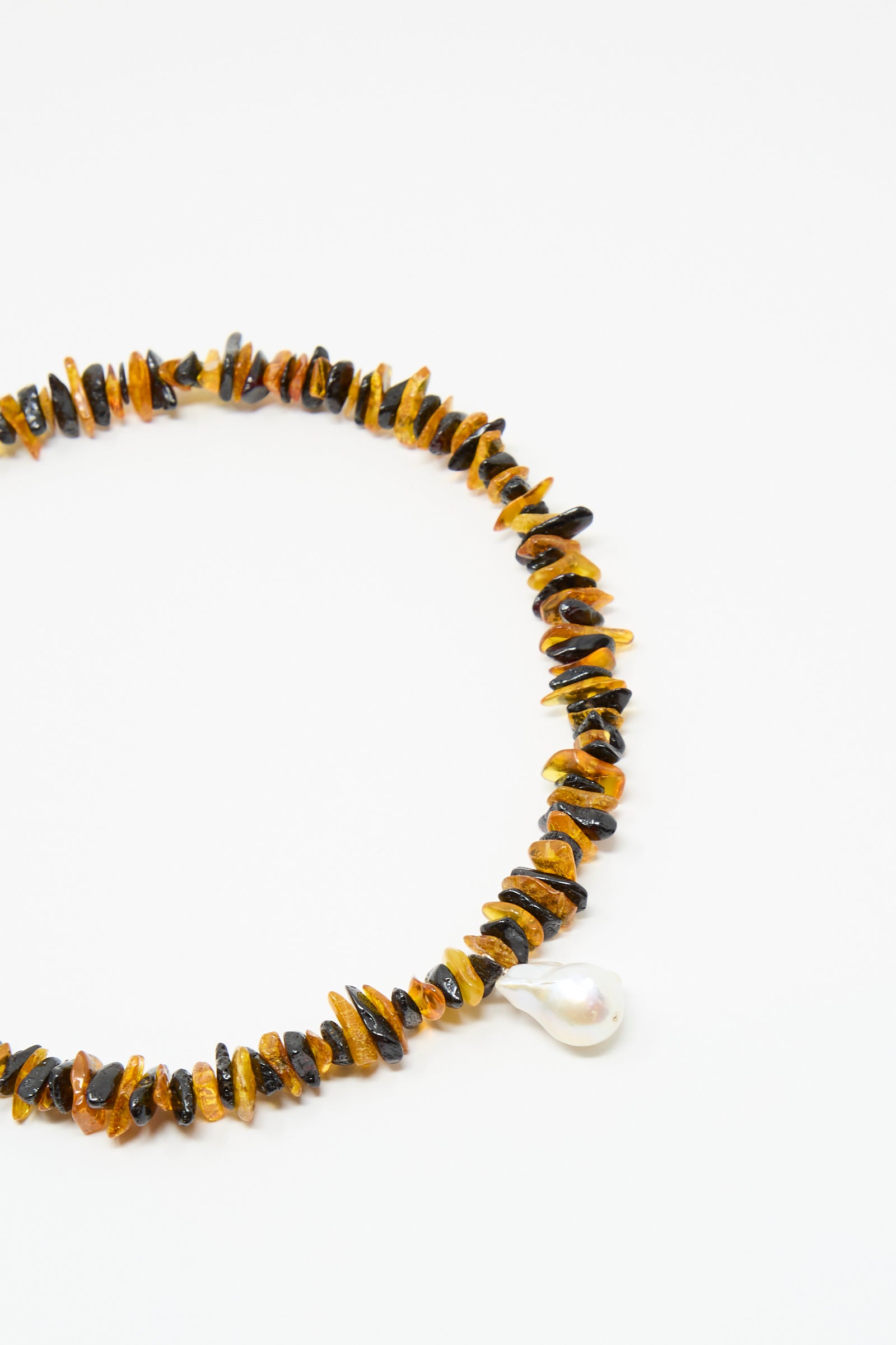 The Santangelo Kitano Necklace in Honey Stripe features irregular Baltic amber and black beads with a teardrop-shaped freshwater pearl pendant, showcased on a white background.