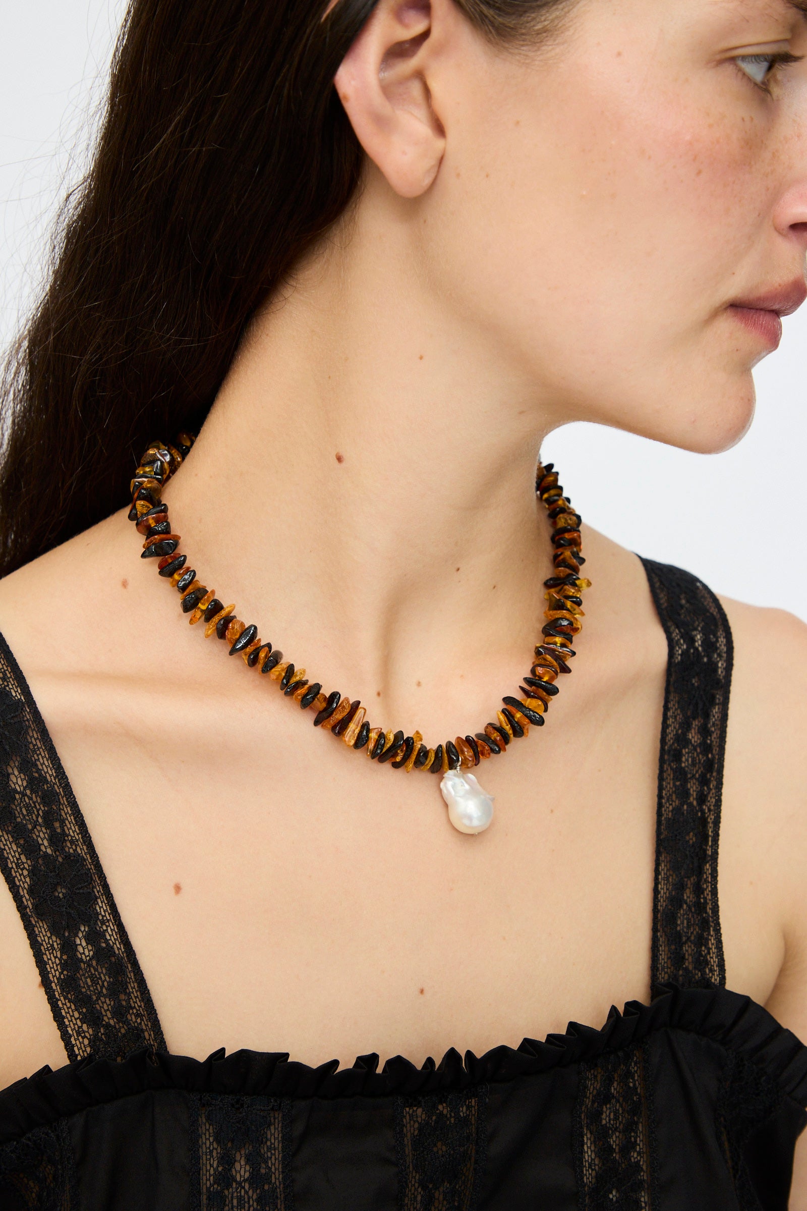 A woman models the Santangelo Kitano Necklace in Honey Stripe, featuring irregular amber stones and a large white pearl pendant.