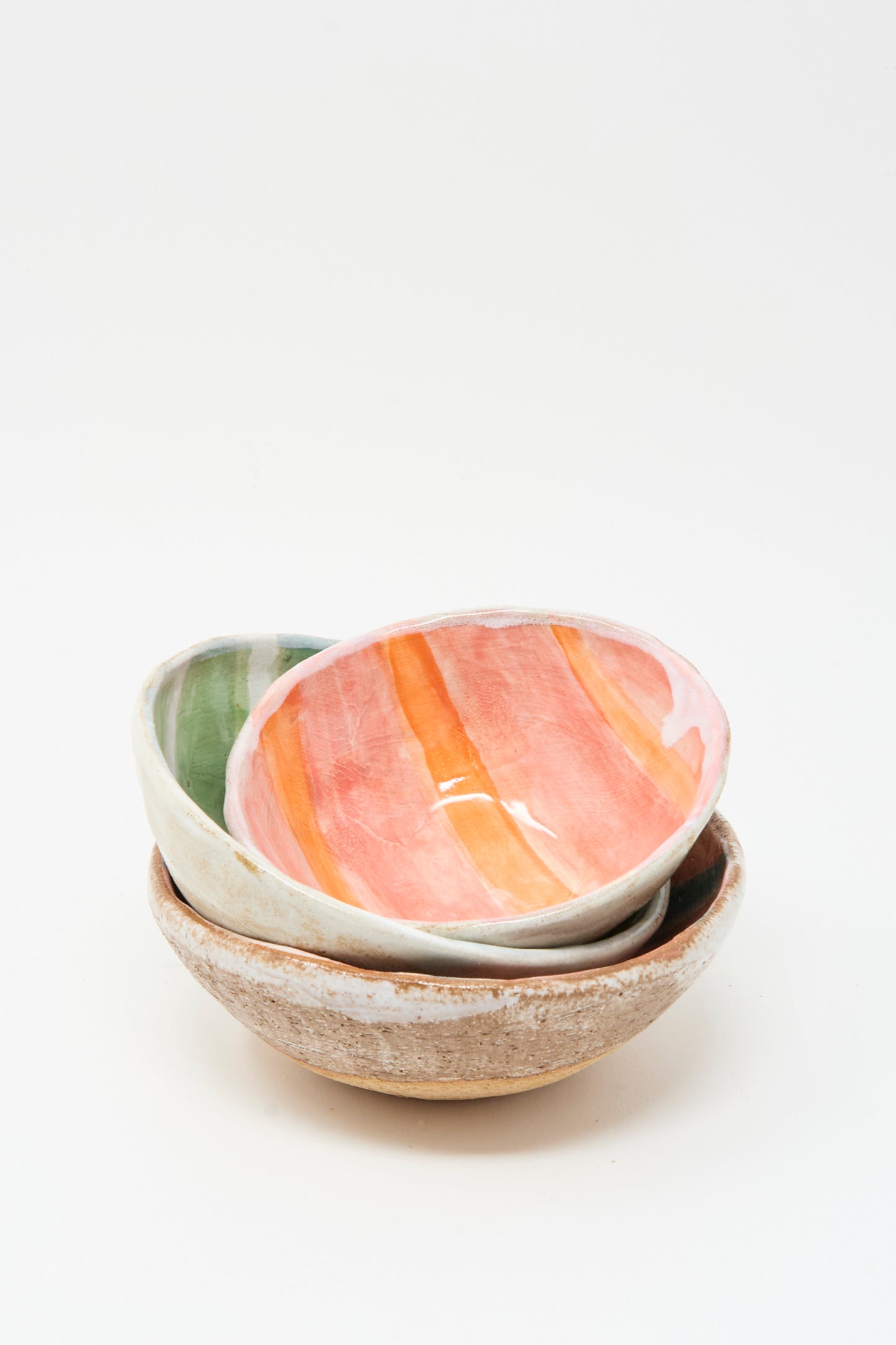 Three ceramic bowls are stacked: the top is orange and pink, the middle is Shino Takeda’s Bowl in Green and White Stripes, and the bottom is plain light brown. 