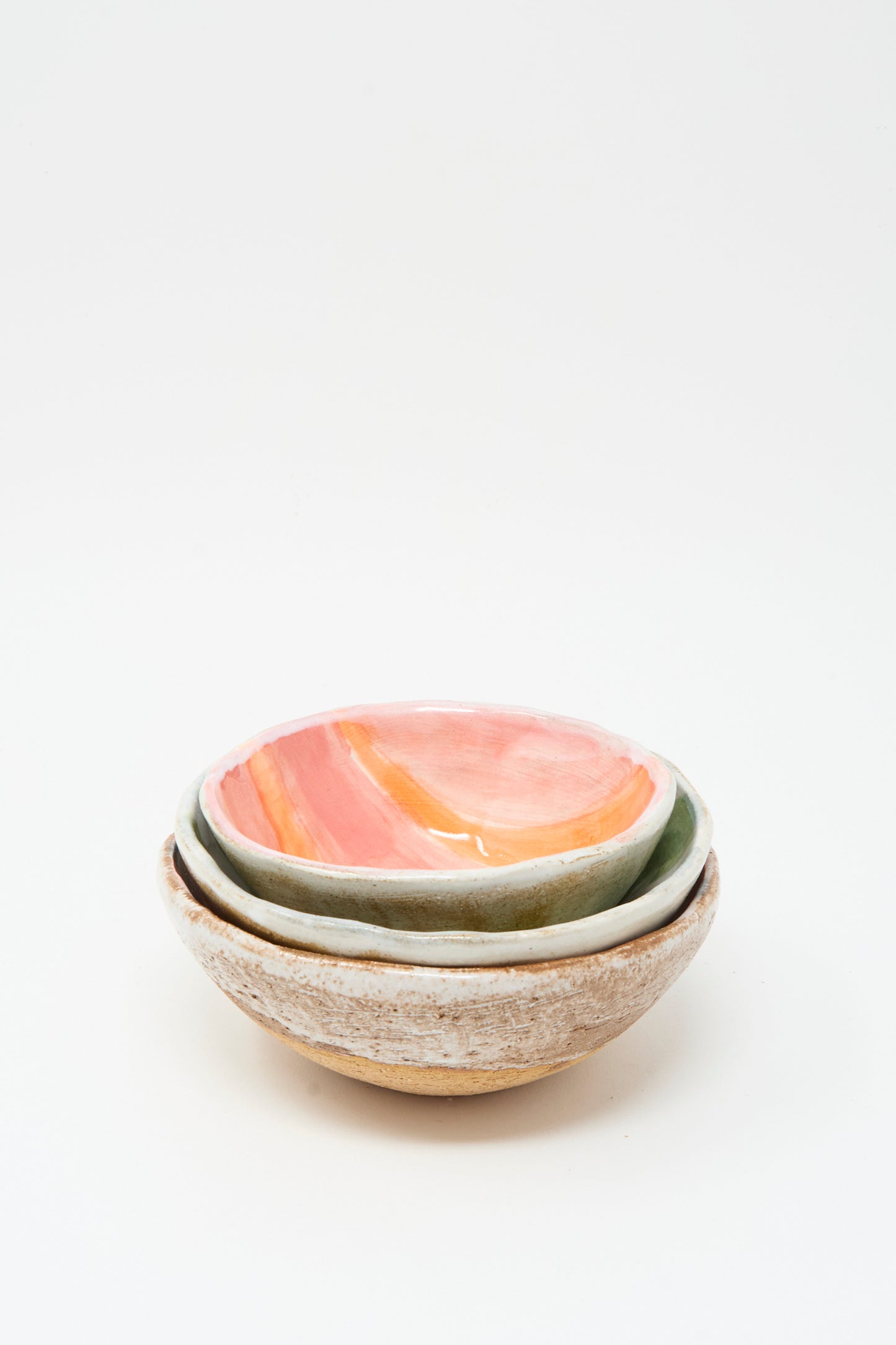 Three handmade ceramic bowls by Shino Takeda are stacked, the top featuring pink and orange glaze, others in earthy tones. Each is crafted in New York; among them is the Bowl in Green and White Stripes.