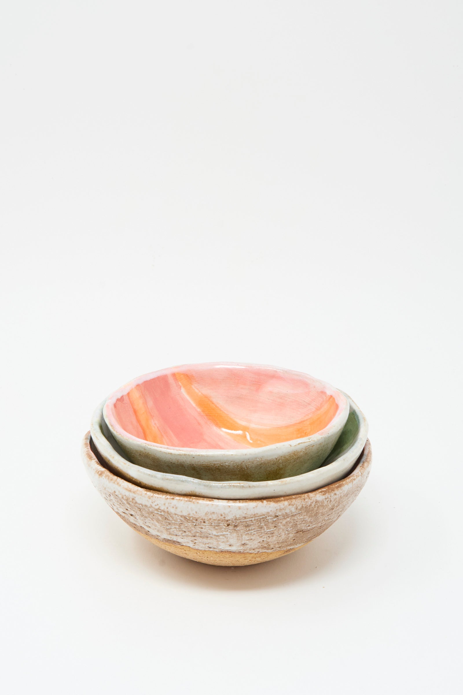 Three handmade ceramic bowls by Shino Takeda are stacked, the top featuring pink and orange glaze, others in earthy tones. Each is crafted in New York; among them is the Bowl in Green and White Stripes.