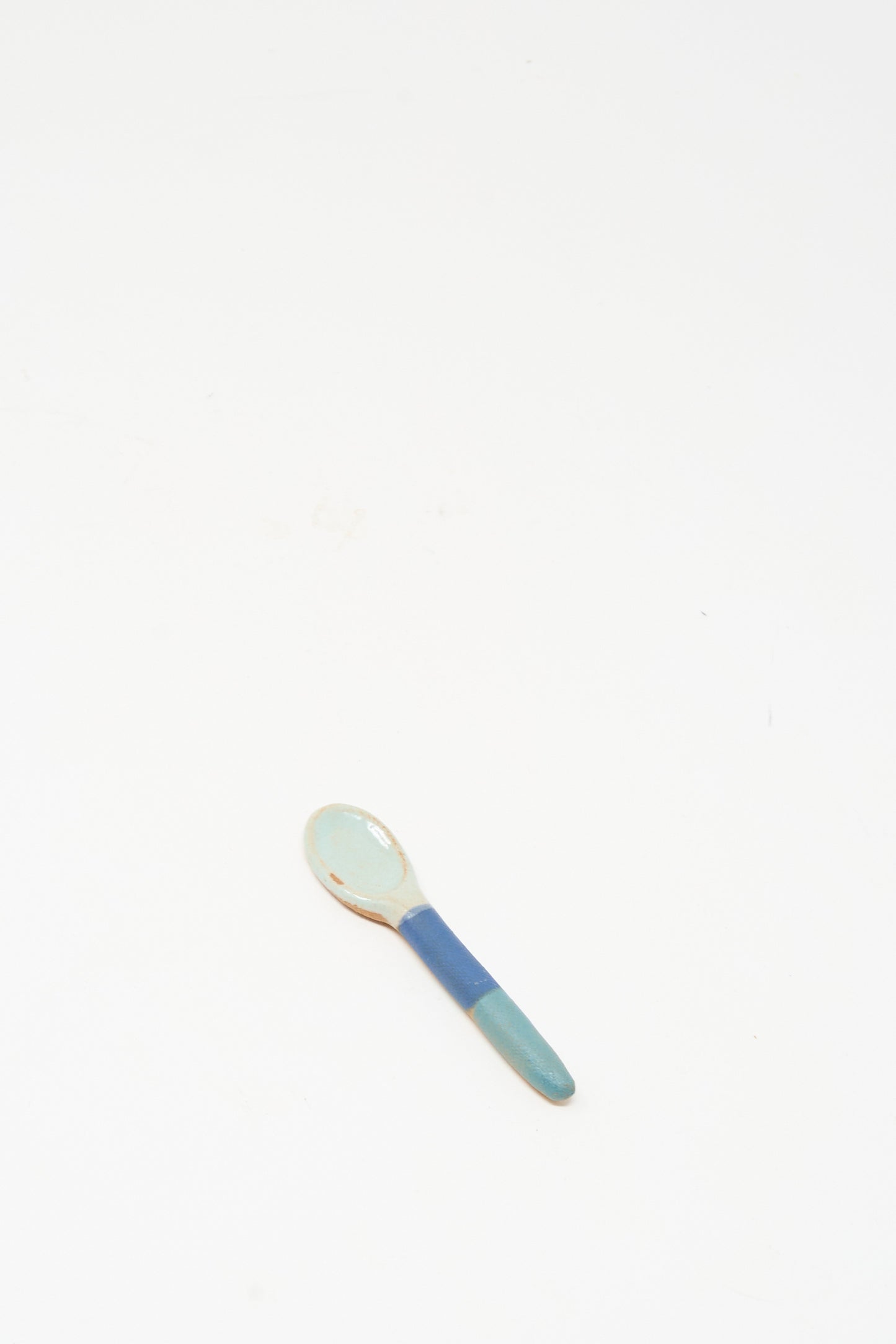 The Shino Takeda Condiment Spoon in Blue Green, a handmade ceramic piece, rests on a plain white surface.