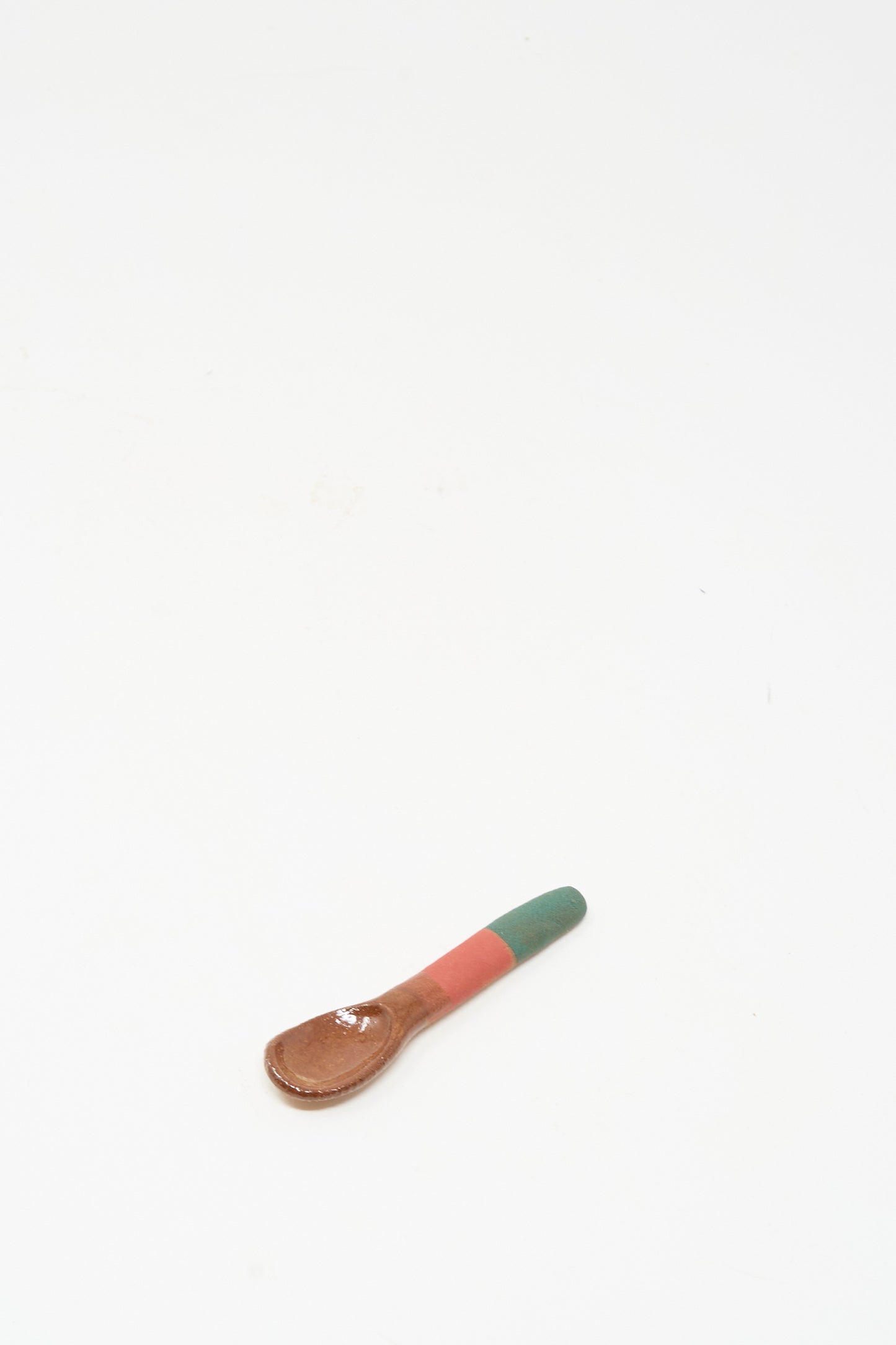 The Shino Takeda Condiment Spoon in Green Red, a handmade wooden piece, rests on a plain white surface.