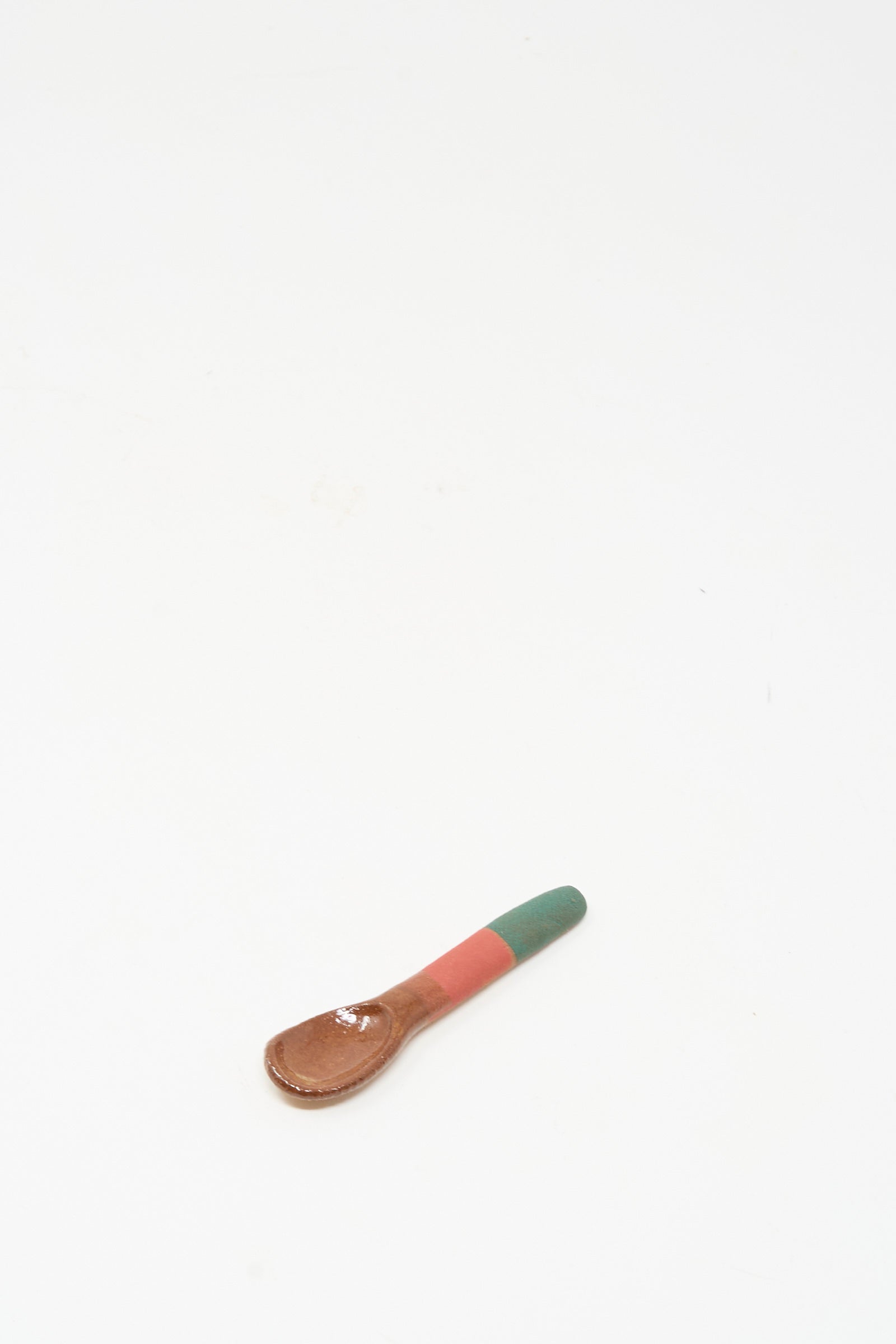 The Shino Takeda Condiment Spoon in Green Red, a handmade wooden piece, rests on a plain white surface.