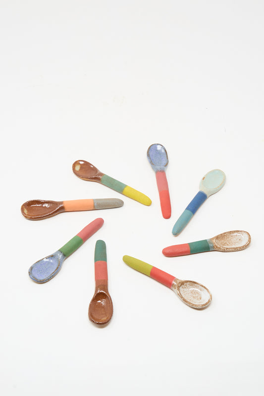The Shino Takeda Condiment Spoon in Lime Red is displayed among eight colorful ceramic spoons arranged in a circle, each featuring a two-tone handle and unique bowl on a white background.