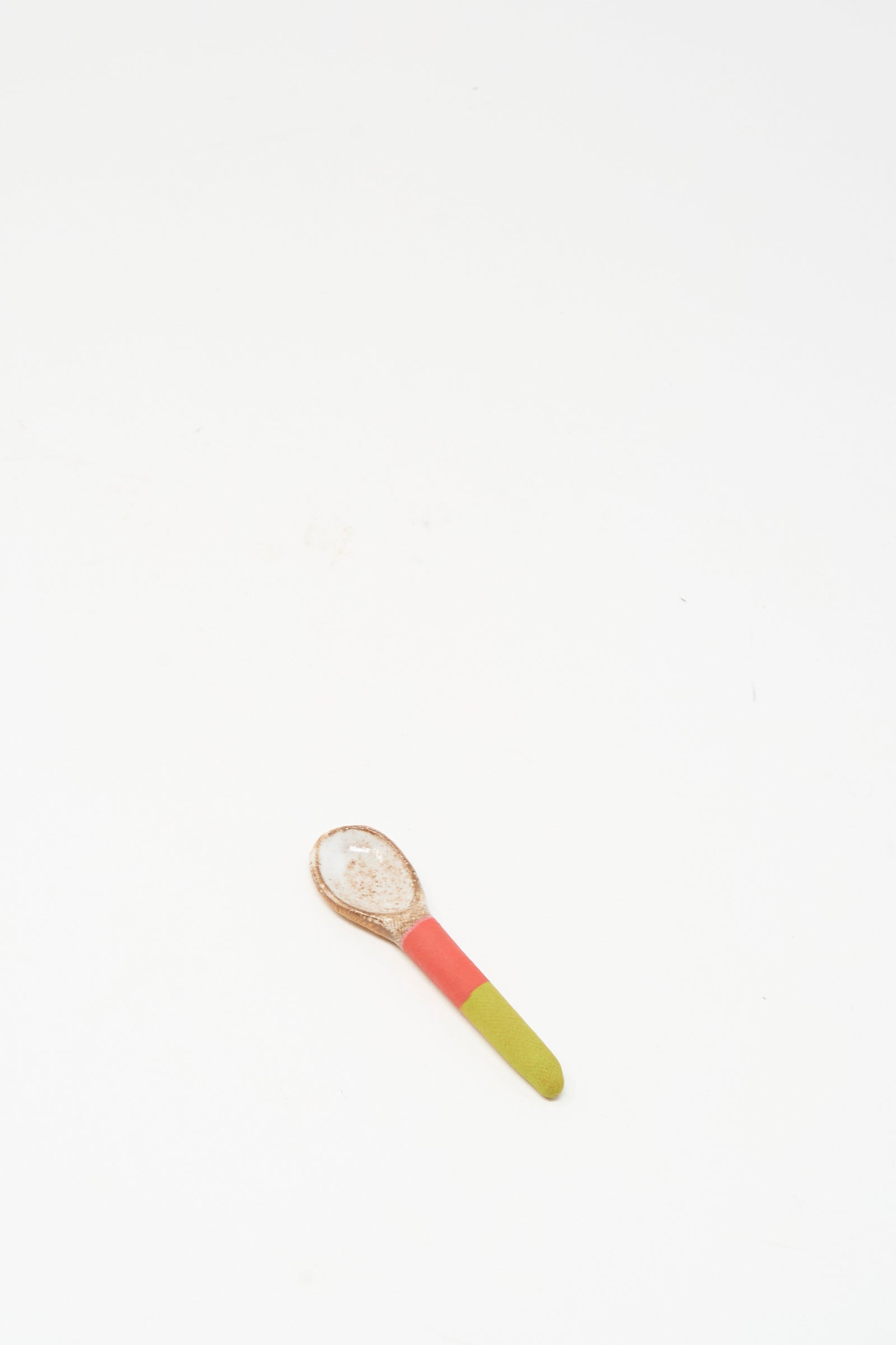 The Shino Takeda Condiment Spoon in Lime Red, a handmade piece, is displayed on a plain white surface.