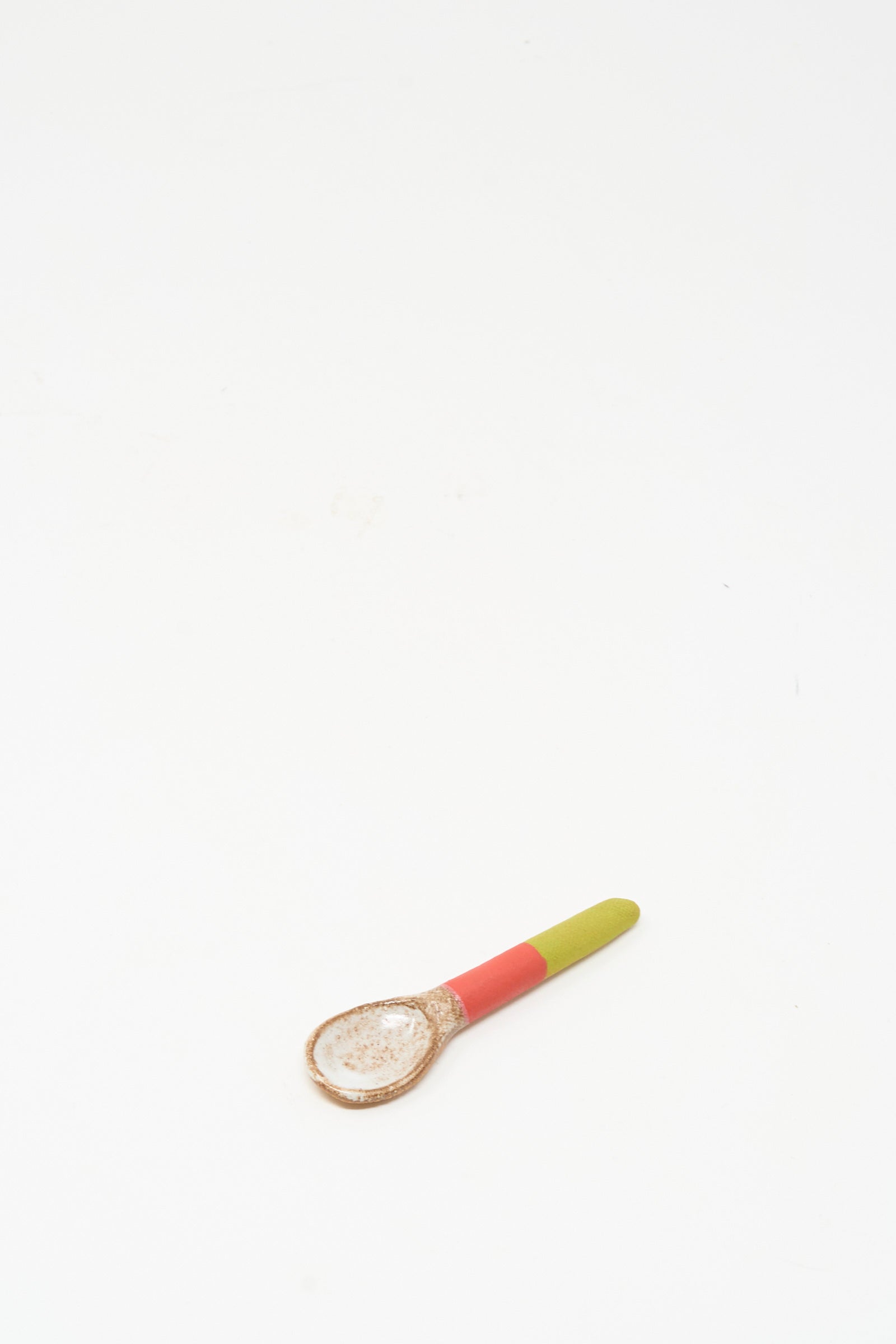 The Shino Takeda Condiment Spoon in Lime Red features a unique handmade ceramic design with a green and red handle, displayed on a white background.