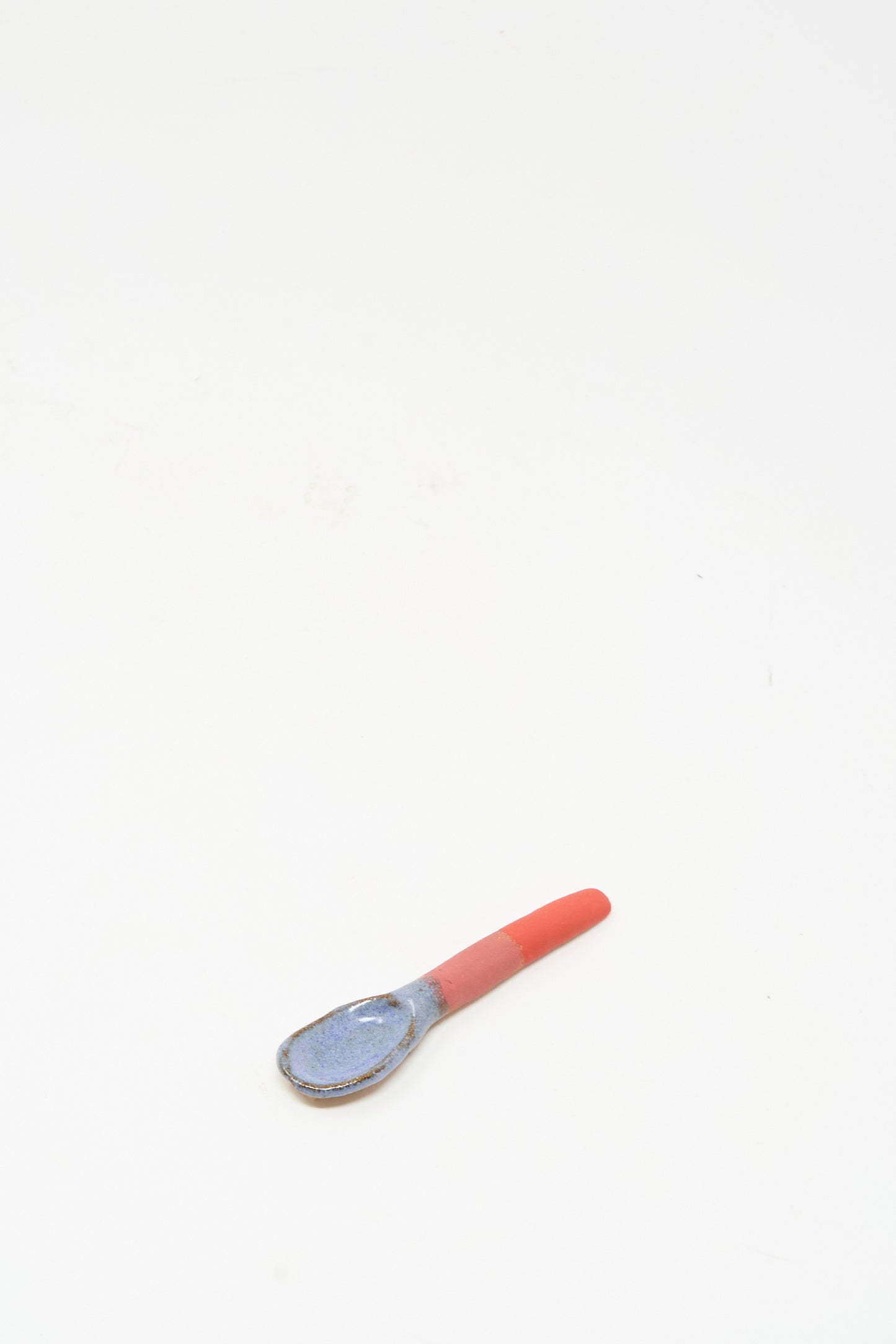 The Shino Takeda Condiment Spoon in Red, a small handmade ceramic piece featuring a vibrant red-glazed handle, rests on a plain white background.