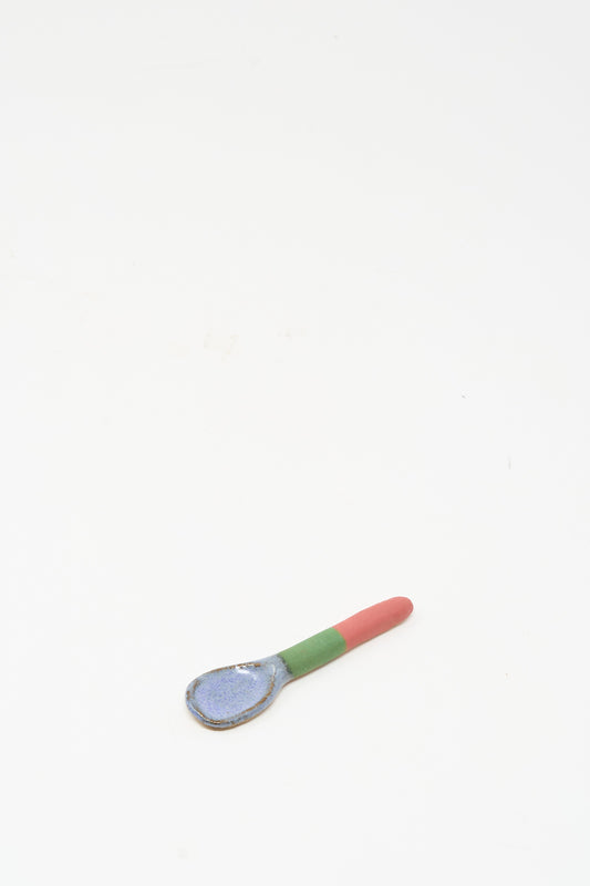 The Condiment Spoon in Red Green II by Shino Takeda—a handmade ceramic piece featuring a blue bowl, green midsection, and red handle—rests on a plain white background. Inspired by New York’s vibrant style.