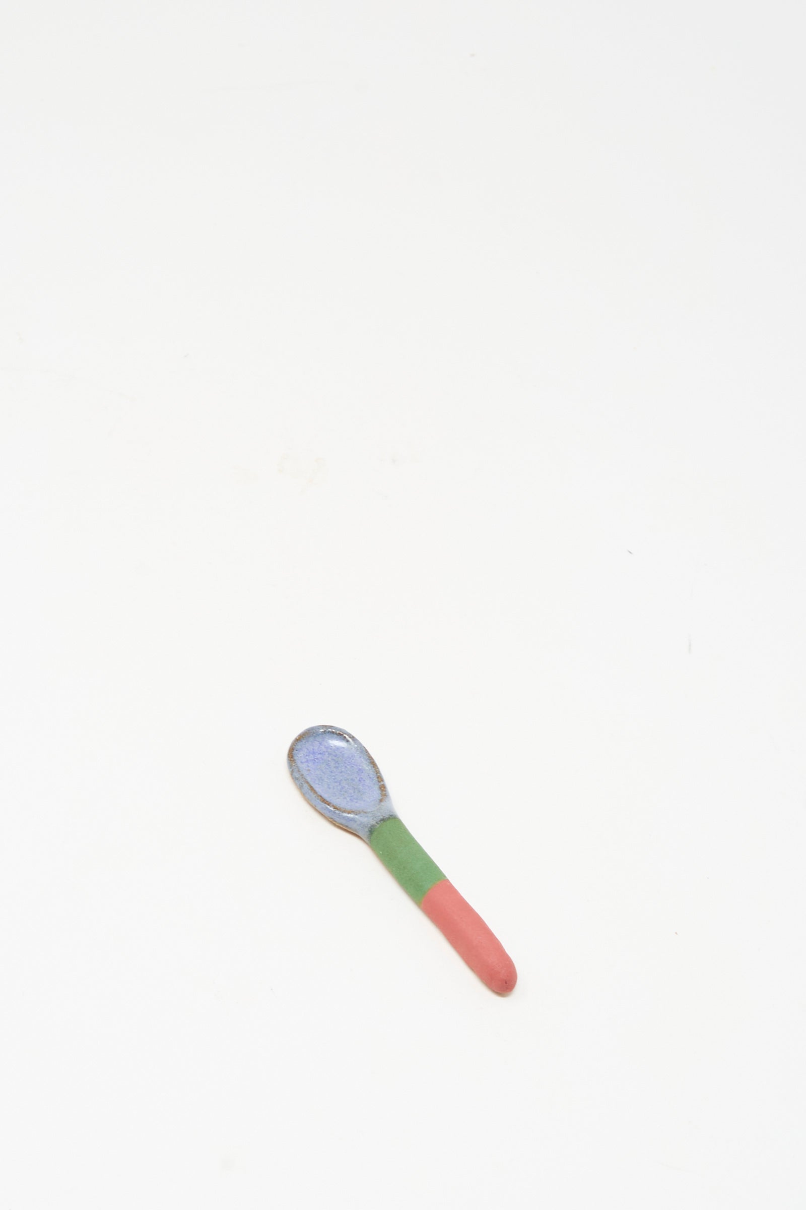 The Shino Takeda Condiment Spoon in Red Green II, a handmade ceramic piece with a blue bowl and a red-green handle, is shown against a plain white background.