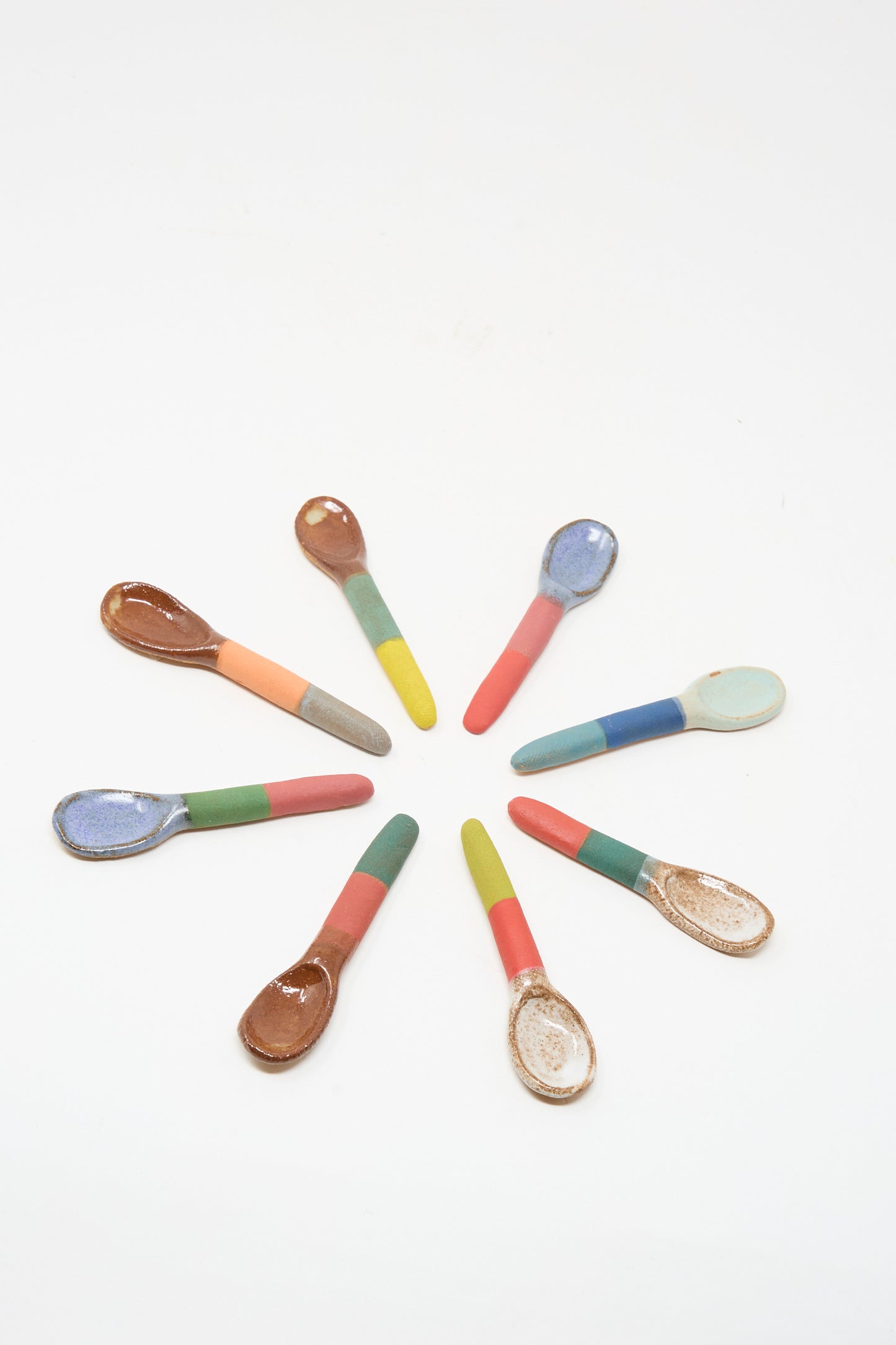 Nine small Shino Takeda Condiment Spoons in Red Green II, each handmade and colorful, are arranged in a circle on a white background, bringing artistic New York flair to your table.