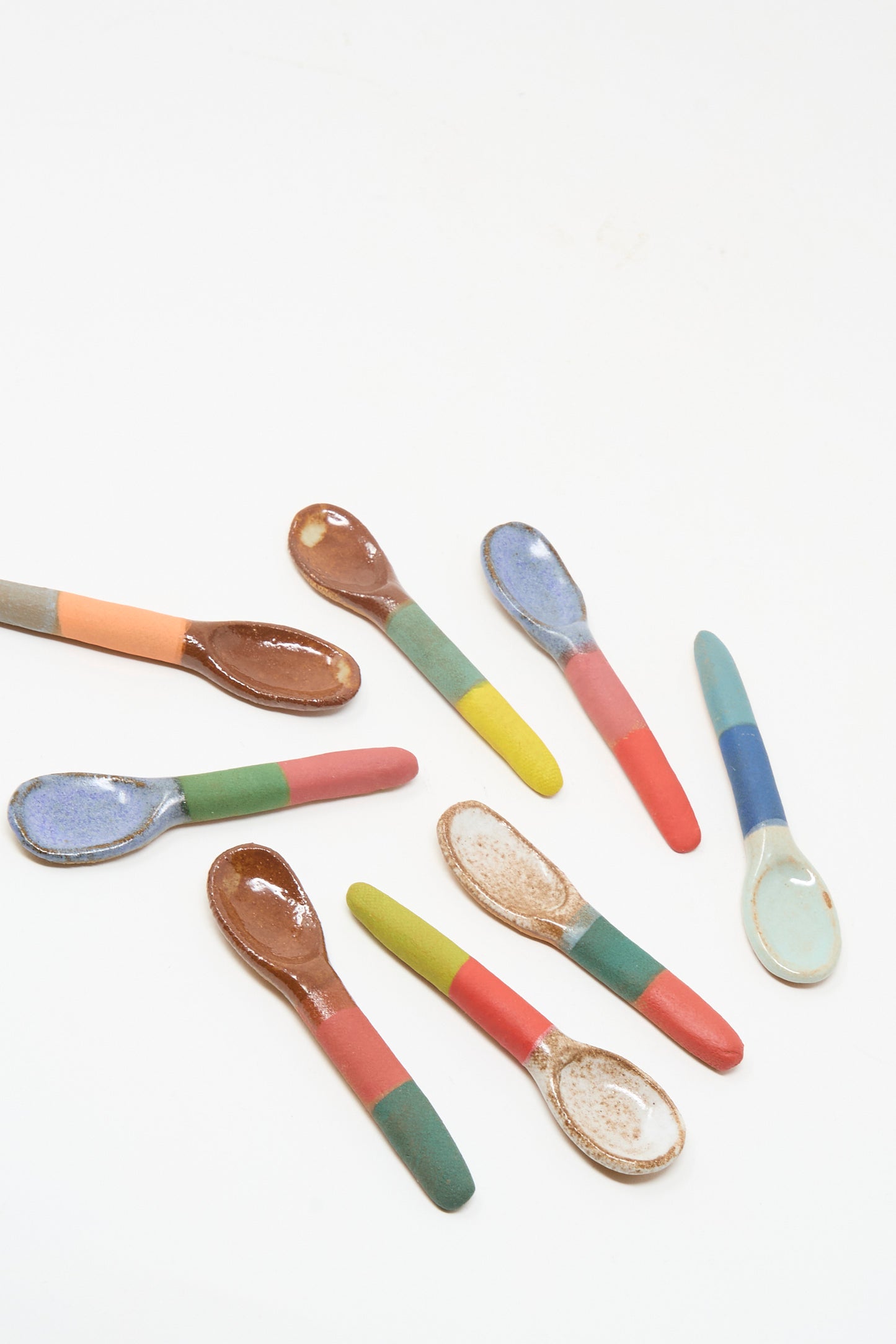 The Shino Takeda Condiment Spoon in Yellow Green features a unique color and glaze combination, with a handmade ceramic design and colorful handle, arranged beautifully against a white background.