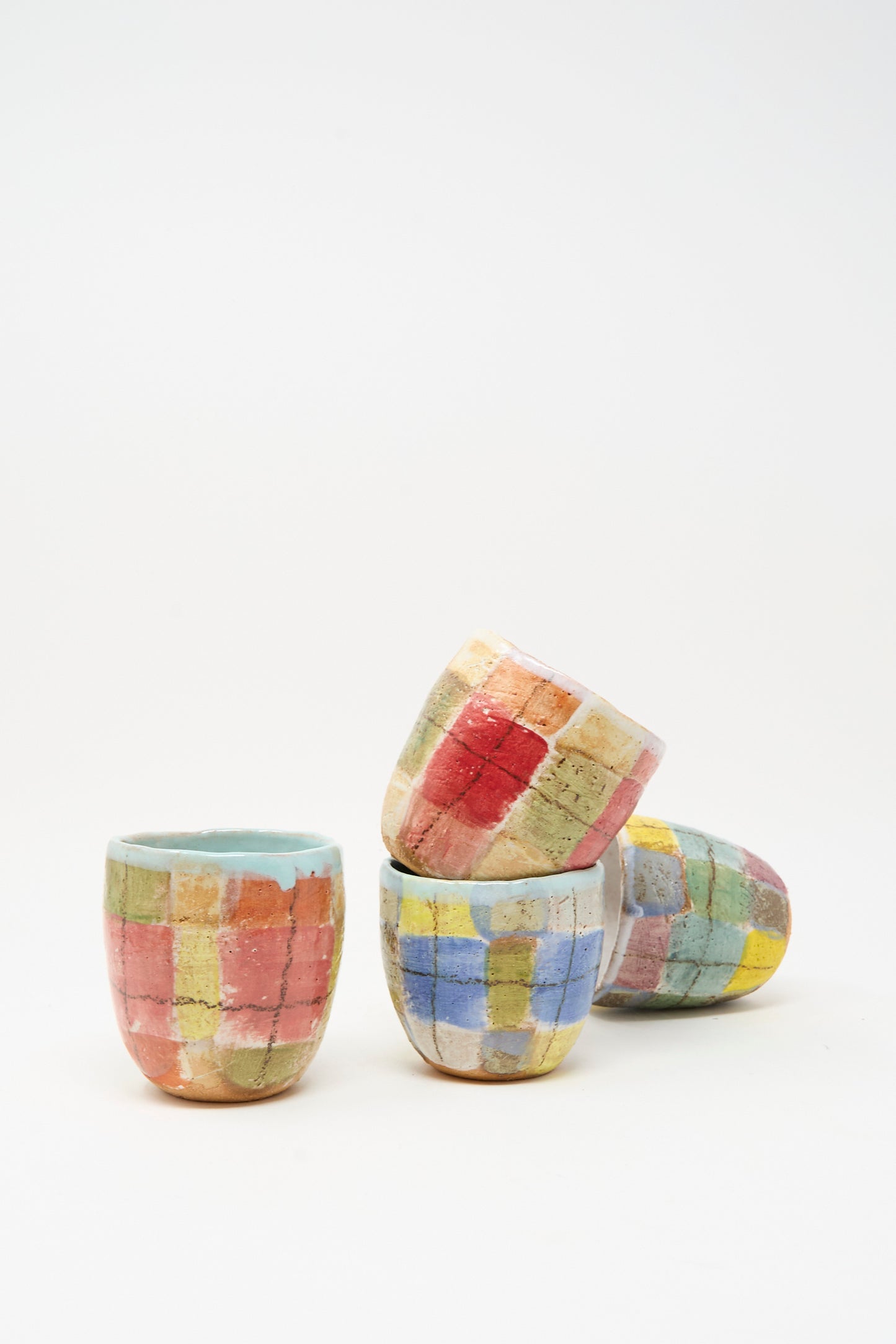 Four small, round ceramic cups from Shino Takeda’s Cup in Blue Plaid I collection are handmade in New York and feature a blue plaid pattern, stacked against a white background.
