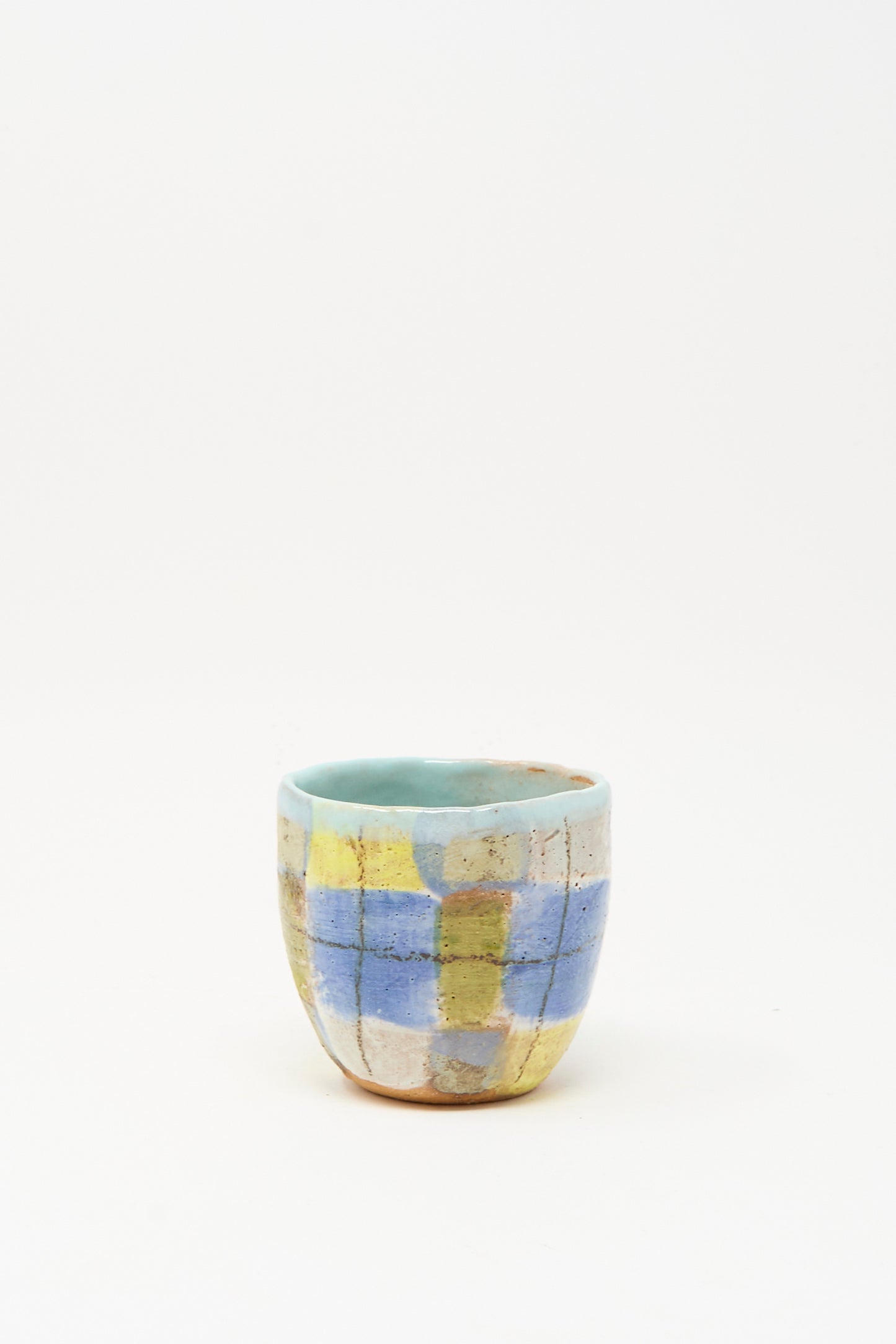 The Cup in Blue Plaid I by Shino Takeda, a small handmade ceramic cup featuring a blue, yellow, and beige checkered pattern, is shown on a plain white background.