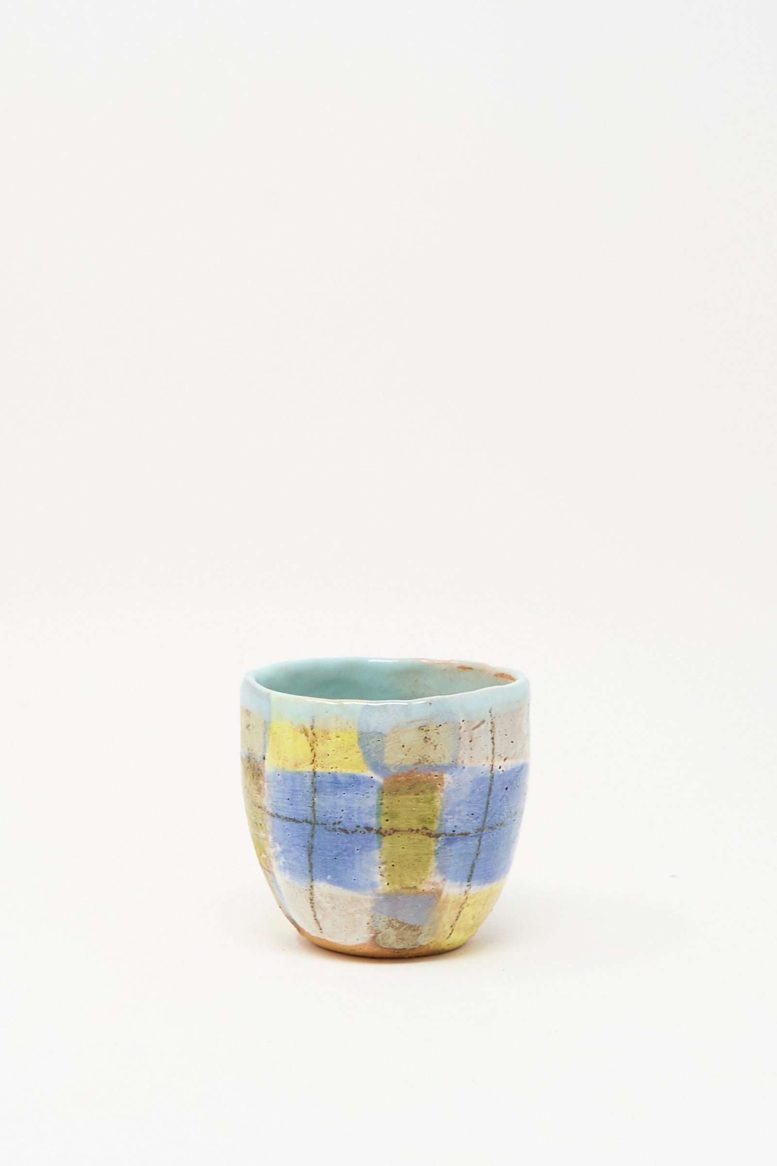 The Cup in Blue Plaid I by Shino Takeda, a small handmade ceramic cup featuring a blue, yellow, and beige checkered pattern, is shown on a plain white background.