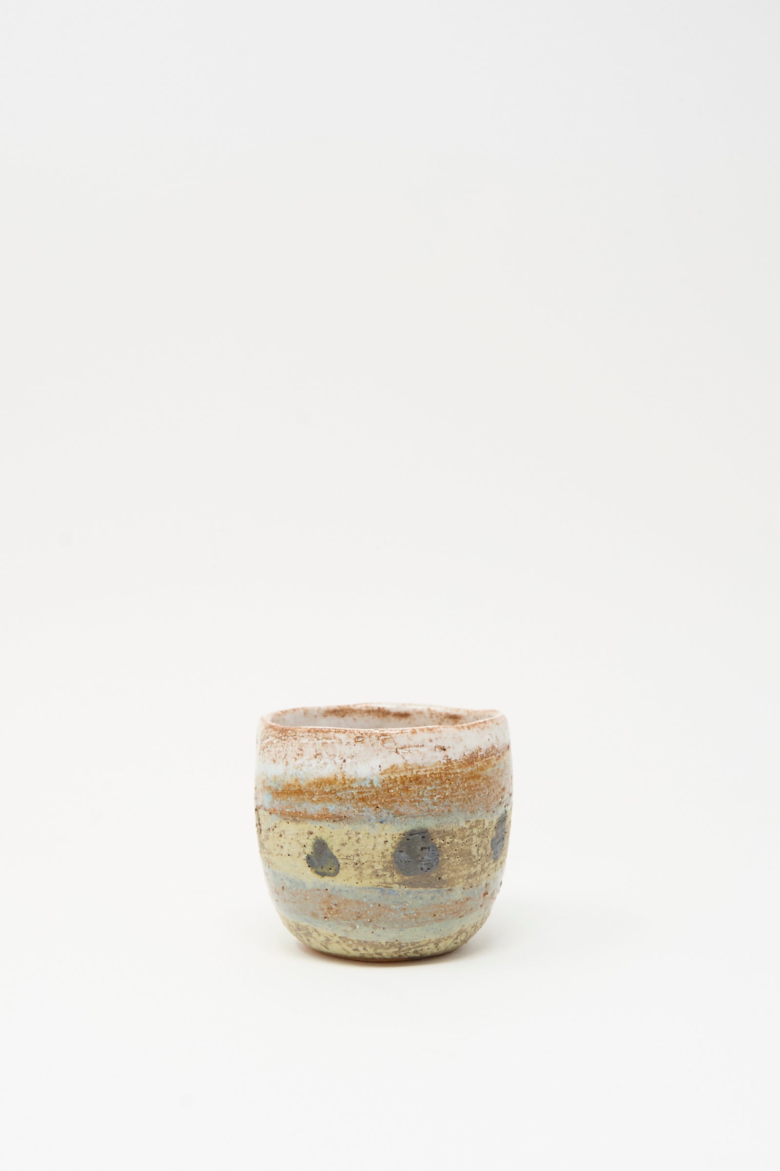 Cup in Dots I by Shino Takeda is a small handmade ceramic cup with earthy tones, a matte finish, and hand-painted dark circular spots. Photographed on a plain white background.