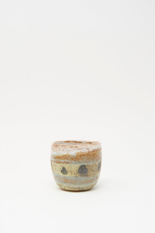 Cup in Dots I by Shino Takeda is a small handmade ceramic cup with earthy tones, a matte finish, and hand-painted dark circular spots. Photographed on a plain white background.