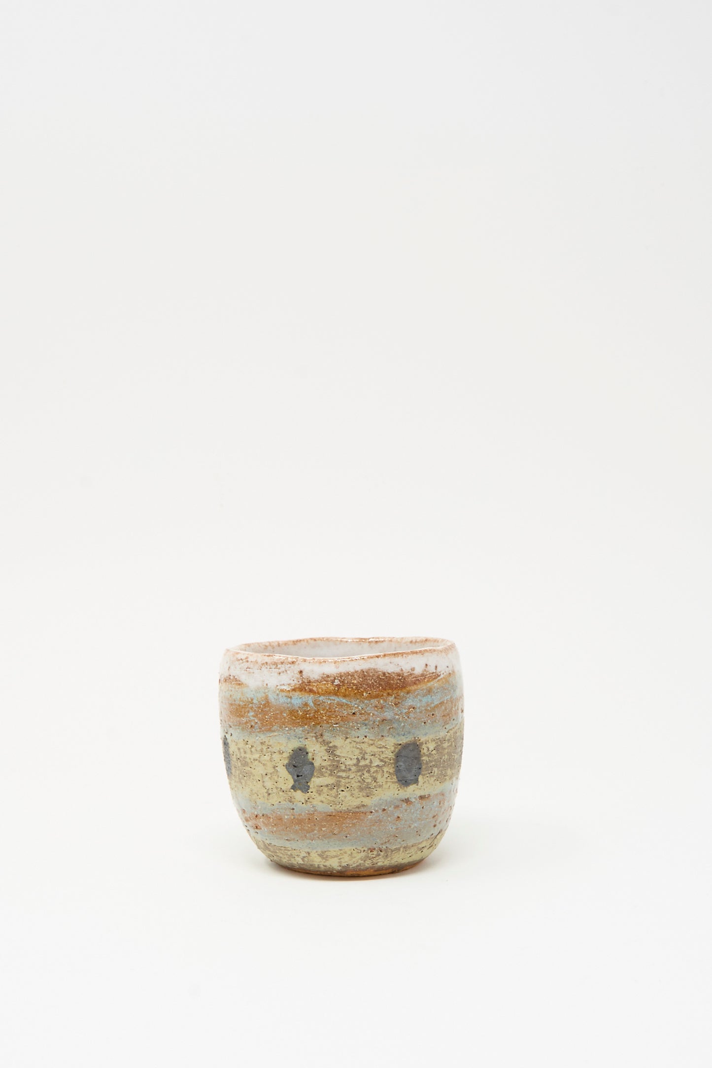The Shino Takeda "Cup in Dots I" is a small, round ceramic cup, hand-painted with earthy beige, brown, and gray bands and a rough texture, displayed against a plain white background.