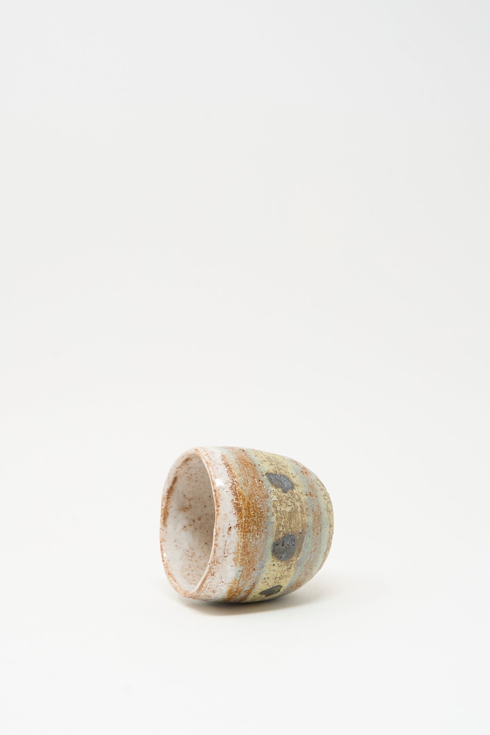 The Cup in Dots I by Shino Takeda is a small, hand-painted ceramic cup featuring a speckled earth-toned glaze, shown resting on its side against a plain white background.