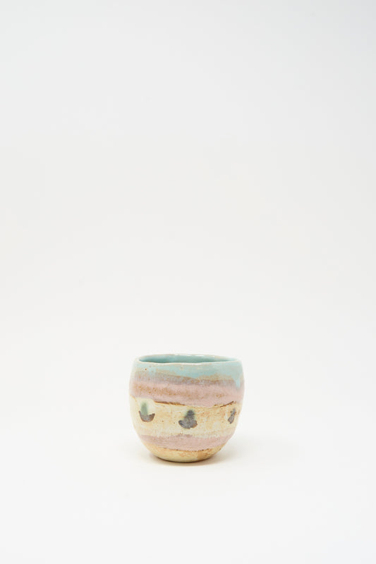 The Cup in Dots II by Shino Takeda is a small ceramic cup from New York, featuring a rounded form, pastel blue-green rim, beige body with hand-painted stripes and dark spots, shown on a plain white background.