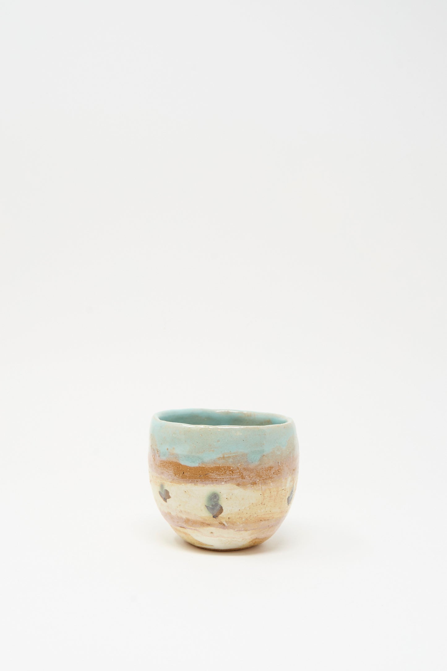 The Cup in Dots II by Shino Takeda is a small, round, hand-painted ceramic cup featuring a mottled beige and brown surface with a light blue rim, shown against a plain white background.